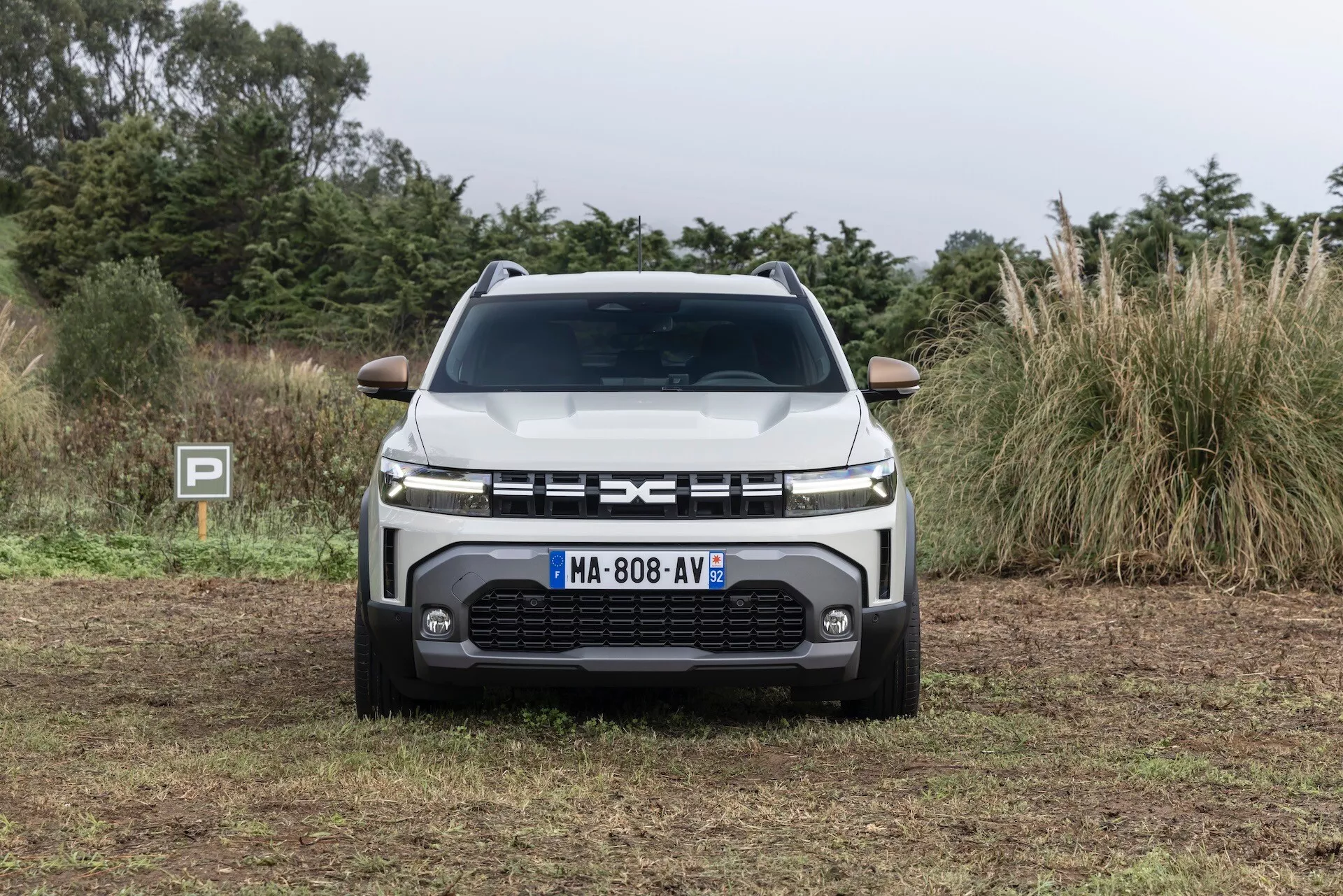 Frontvy av Dacia Duster 3:e generationen 2024 som visar grillen, LED-strålkastare, avancerade sensorer och robust stötfångardesign mot en naturlig bakgrund