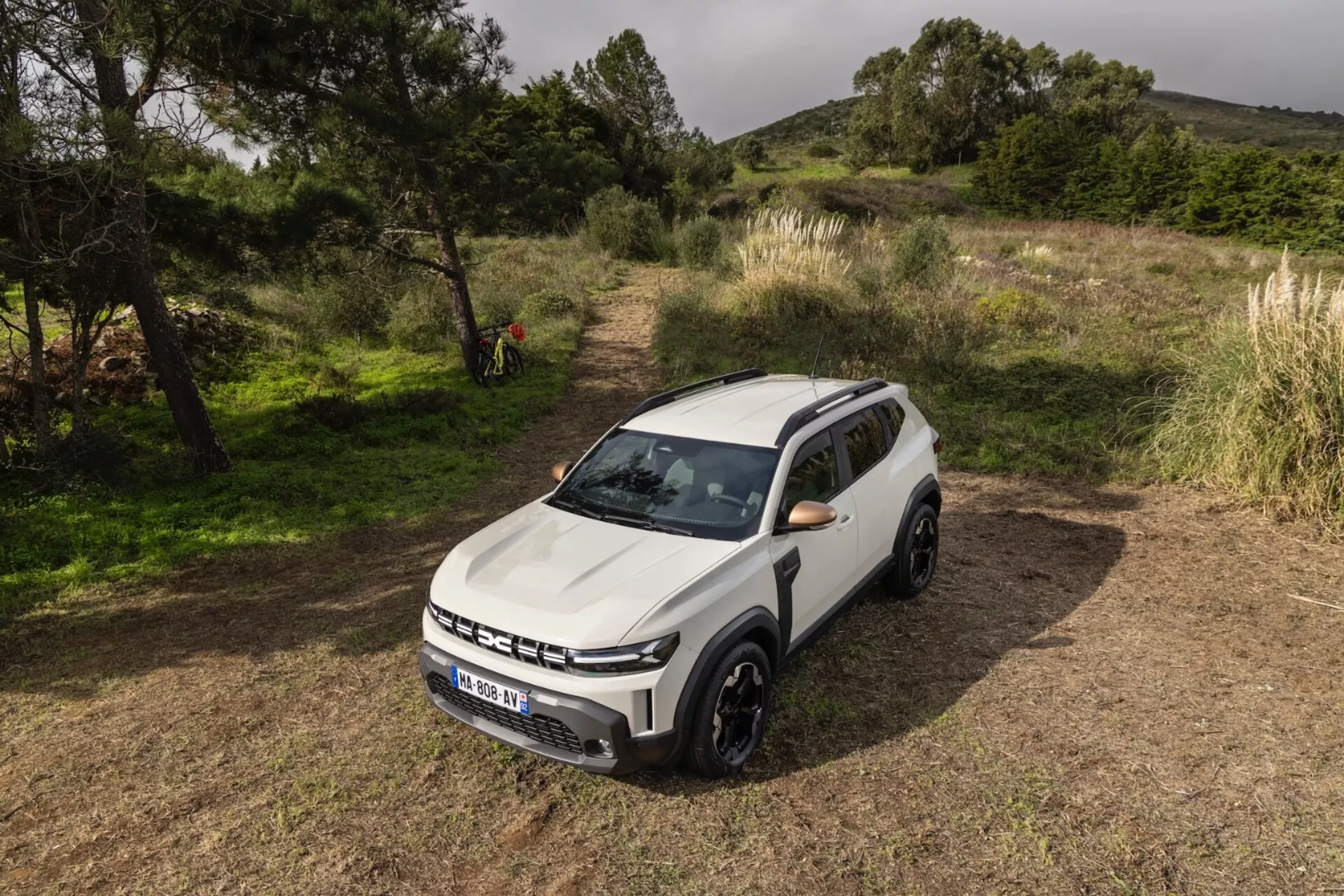 Vit SUV Dacia Duster 2024 parkerad på ojämn gräsmark som visar framifrån och tre fjärdedelars vy som framhäver grilldesign, LED-dagsljus och avancerade förarassistentfunktioner