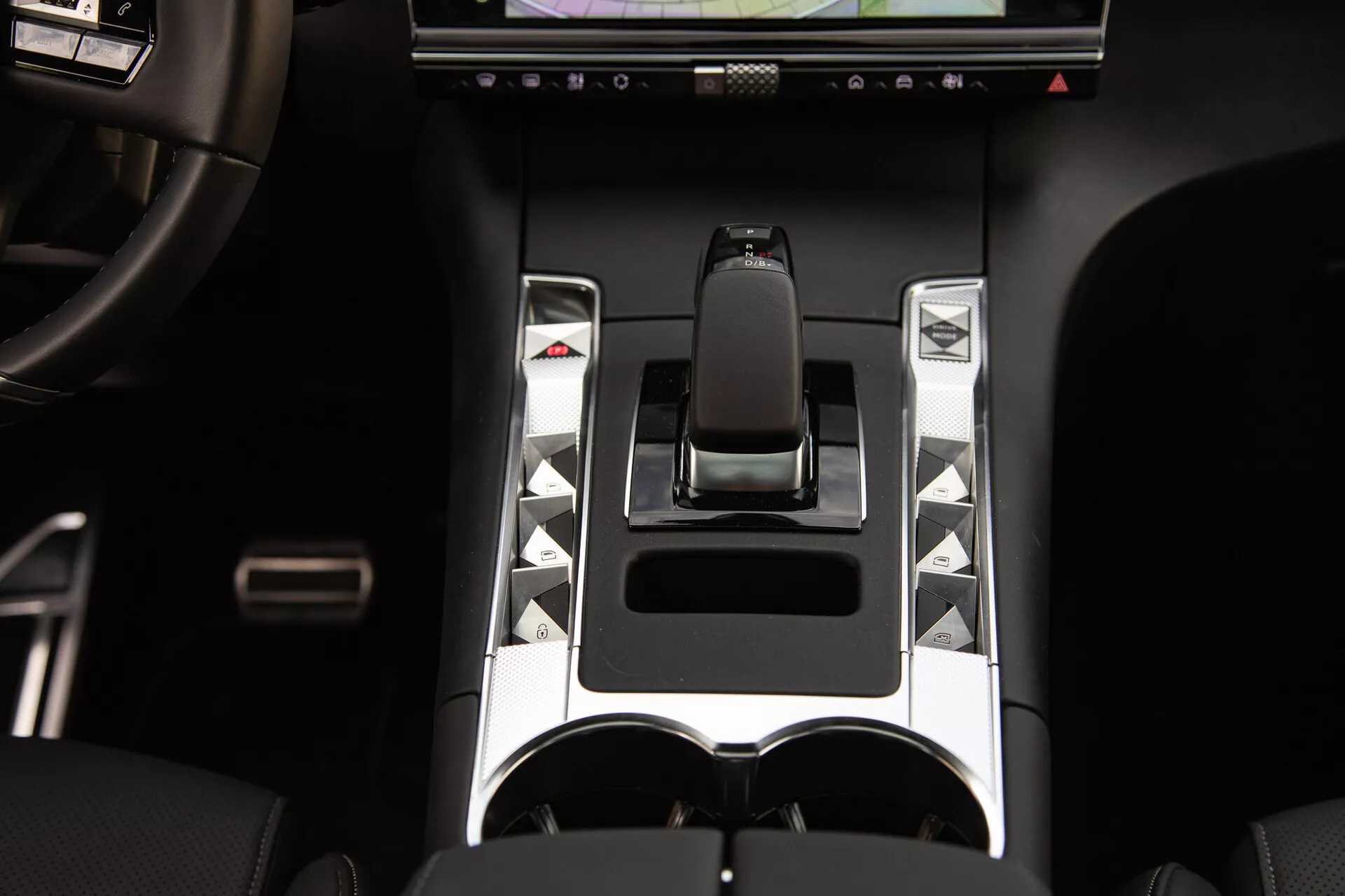 Detaljerad vy av mittkonsolen i DS Automobiles DS-7 2022 med ergonomisk växelspak, metalliska accenter, unika kontrollknappar, pekskärm och dubbla mugghållare, vilket framhäver avancerade fordonkontrollelement och lyx designelement.