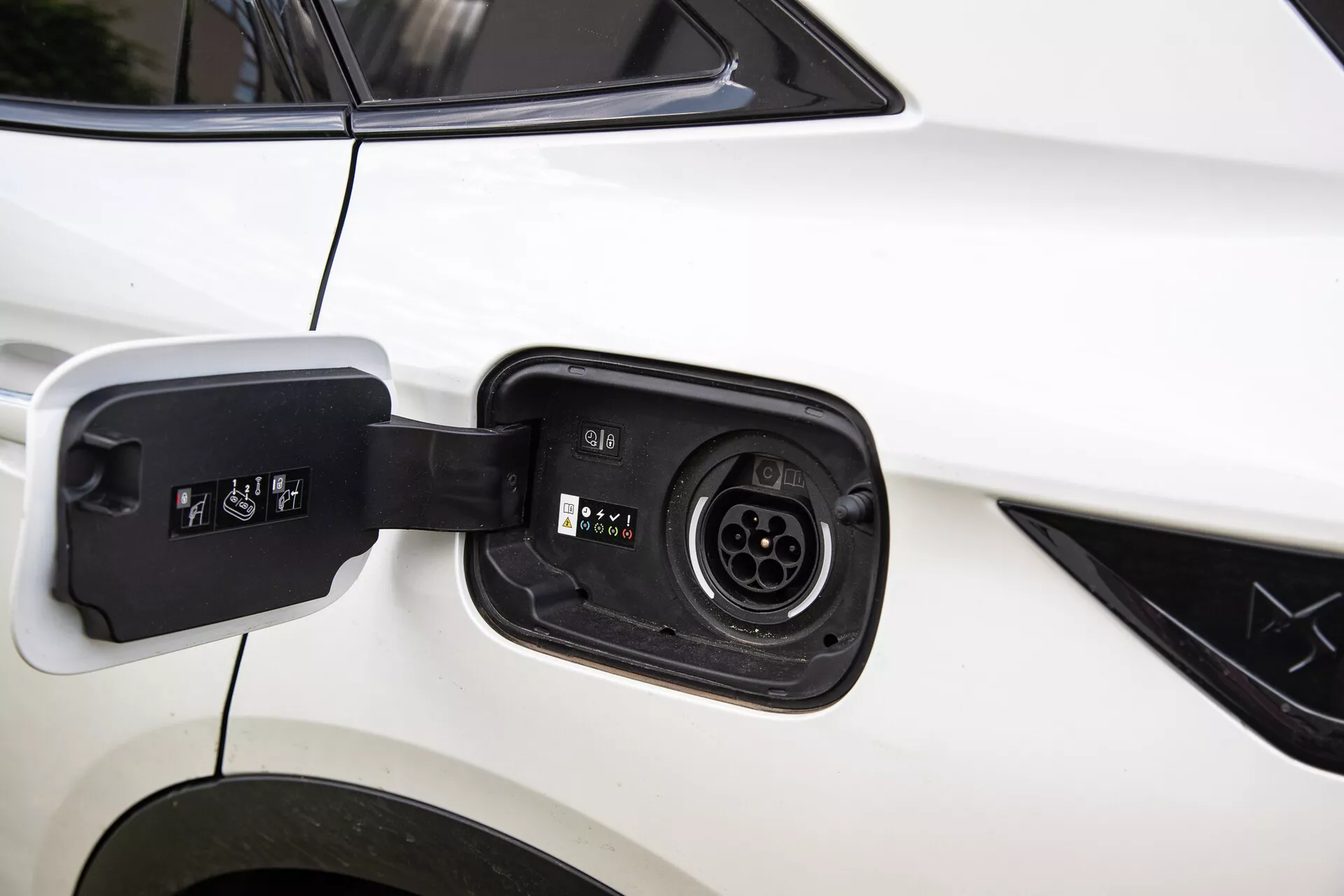 Närbild av laddningsporten på DS Automobiles DS-7 2022 elhybrid, som visar kompatibilitet med flera laddningskontakter mot en vit bilkarossbakgrund