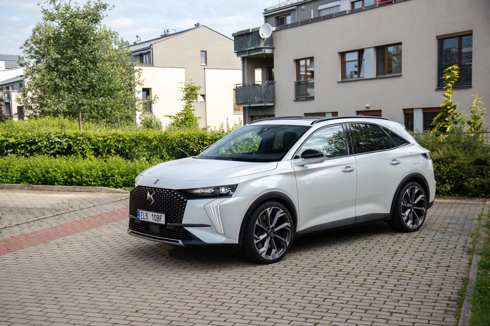 Trekvarts framsida av en DS Automobiles DS-7 2022 crossover parkerad på en bostadsgata belagd med tegel, som visar dess moderna design inklusive en distinkt frontgrill, slanka LED-strålkastare, skulpterad huva, stora legeringshjul och en sportig sidoprofil med integrerade blinkers på dörrmonterade sidospel under naturligt dagsljus.