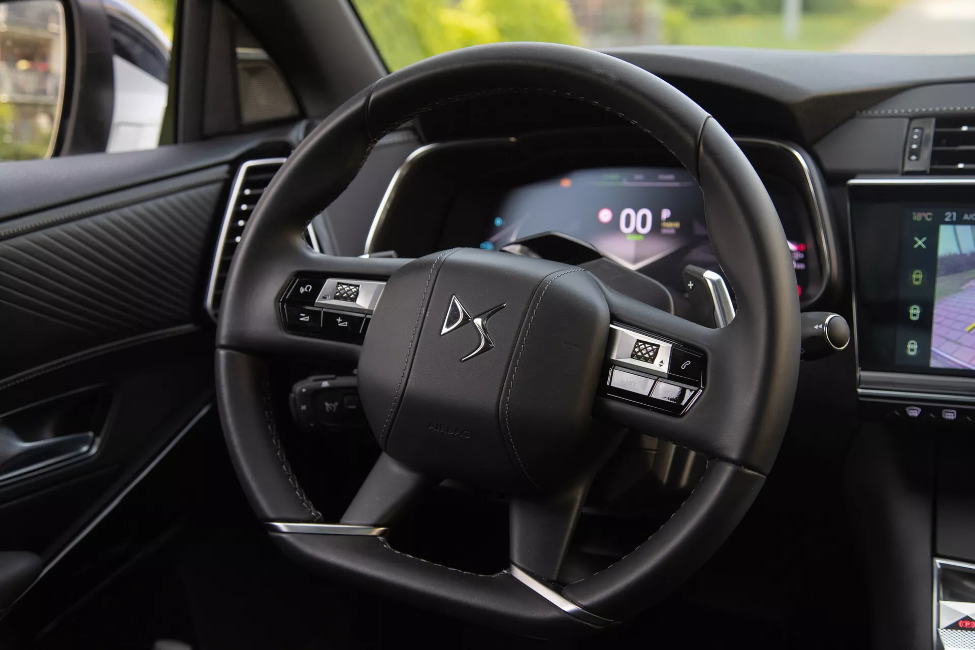 Interiörvy av DS Automobiles DS-7 2022 som visar ratten med multifunktionella knappar och digital instrumentpanel, inklusive paddelskiftare och del av infotainmentsystemet som visar navigering