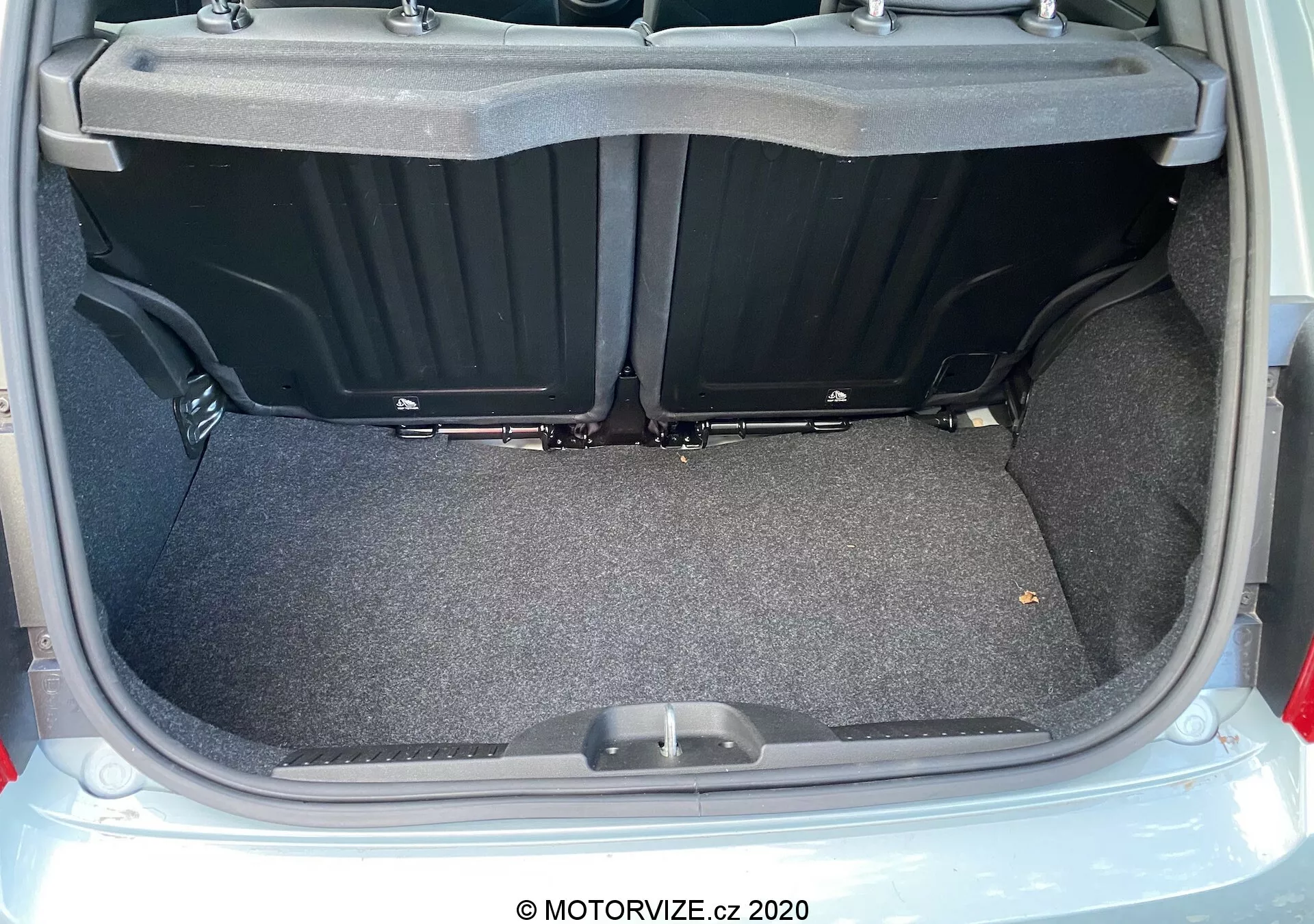 Närbild av bagageutrymmet i en Fiat 500 från 2015 sett bakifrån med öppet lock, som visar ett mattaförsett, plant lastutrymme med plastfack på sidorna och ett handtag på bagagerumsgolvet. Bilden framhäver bagageutrymmets rymlighet, användbarhet och rena, välbelysta skick.