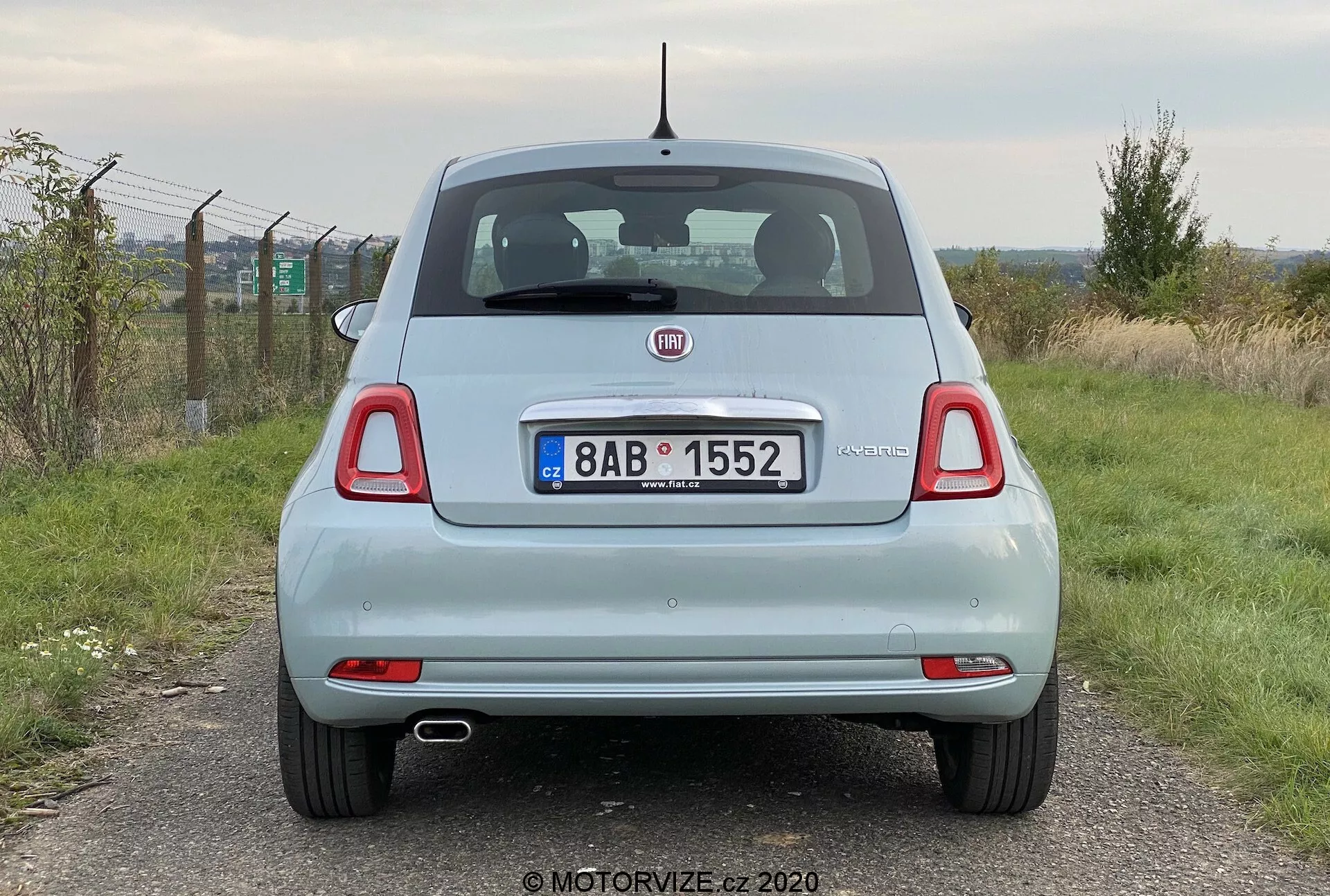 Bakifrån vy av en ljusfärgad Fiat 500 hatchback från 2015, tagen i ögonhöjd och visar bilens hela bredd. Bilden lyfter fram bakluckan med varumärkeslogotyp och modellnamn, bakre stötfångare, bakljus, bakrutetorkare och dubbla avgasrör. Reflektorer nära stötfångarens hörn och antennen på taket är också synliga. Registreringsskylten och omgivningen är delvis synliga men fokus ligger på fordonet.