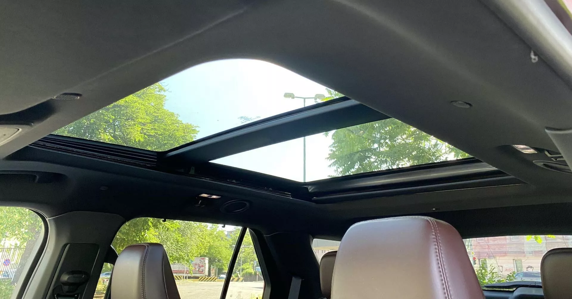 Interiörvy av en 2019 Ford Explorer med fokus på panoramataket från baksätesområdet. Taket sträcker sig från framdelen mot bakdelen med en stor glaspanel som släpper in mycket naturligt ljus, kompletterat med en öppen infällbar solskärm. Den främre delen av taket innehåller takkonsolens kontroller och en läslampa. Den mörka innertaket kontrasterar med de ljusare lädersätena, som visar en modern design och lyxiga interiördetaljer.