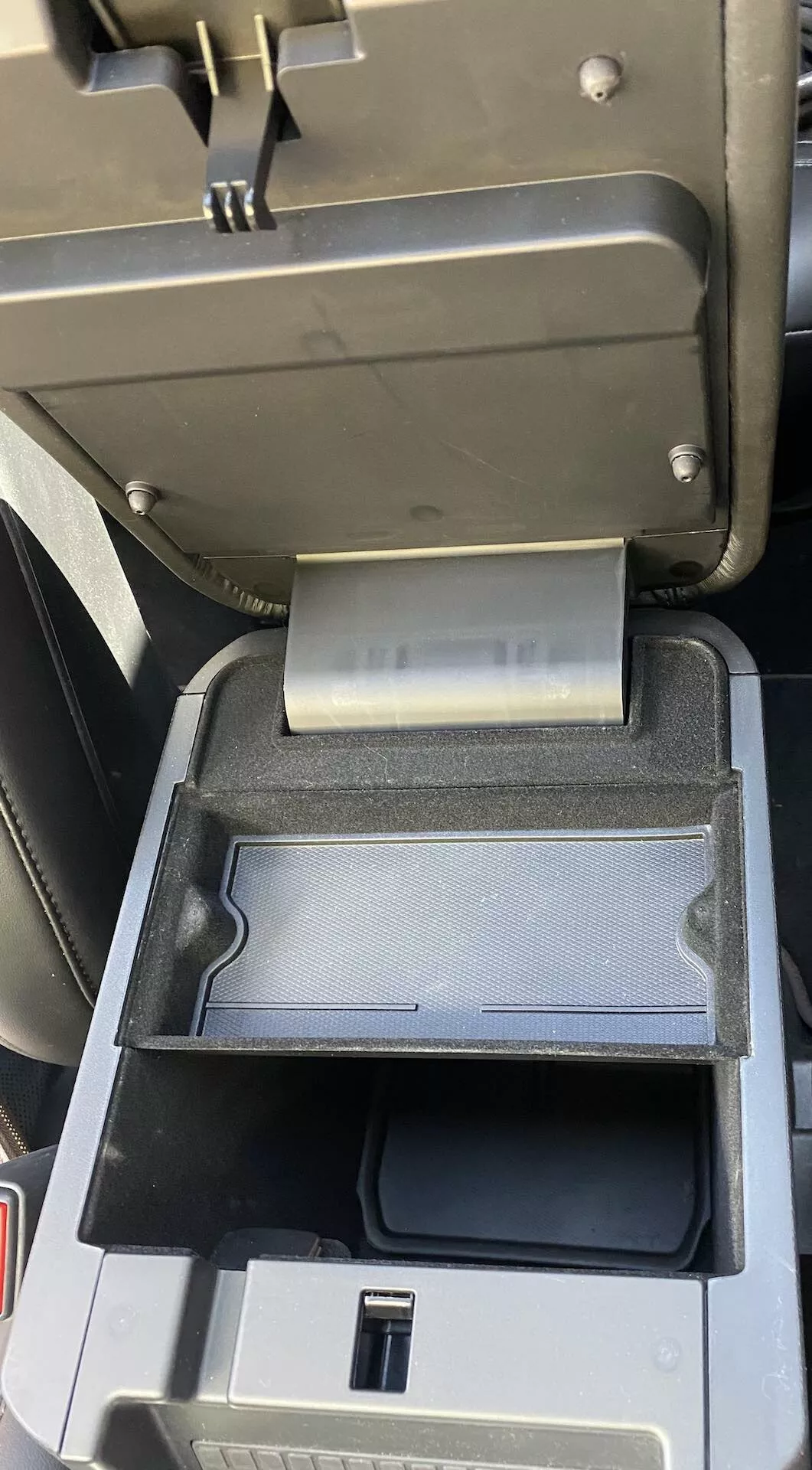 Närbild av interiören i en 2019 Ford Explorer med detalj av mittkonsol som visar öppen mittarmstöd med skjutbart sekundärt fack bakåt, vilket avslöjar USB-port och djupare förvaringsutrymme i svart plastfinish.