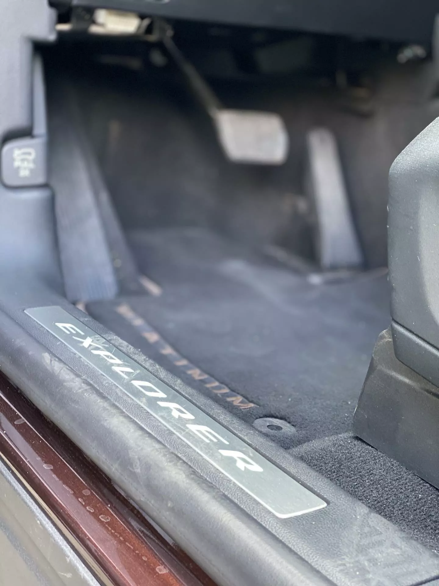 Närbild av interiören i en Ford Explorer 2019 SUV, som specifikt visar dörrtröskelområdet med en borstade metallplatta ingraverad med 'Explorer'-logotypen. Bilden framhäver tröskeln där passagerare kliver in, med mörk golvmatta, vädertätning och mjukt naturligt ljus.