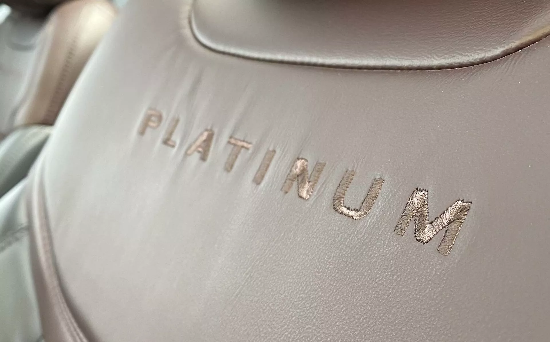 Närbildsdetalj av interiörklädseln i en Ford Explorer 2019, med ordet 'PLATINUM' präglat på en slät tyg- eller läderyta, med en lätt diagonal vinkel. Texten är i fokus, med mjuk, jämnt fördelad belysning och ett grunt skärpedjup.