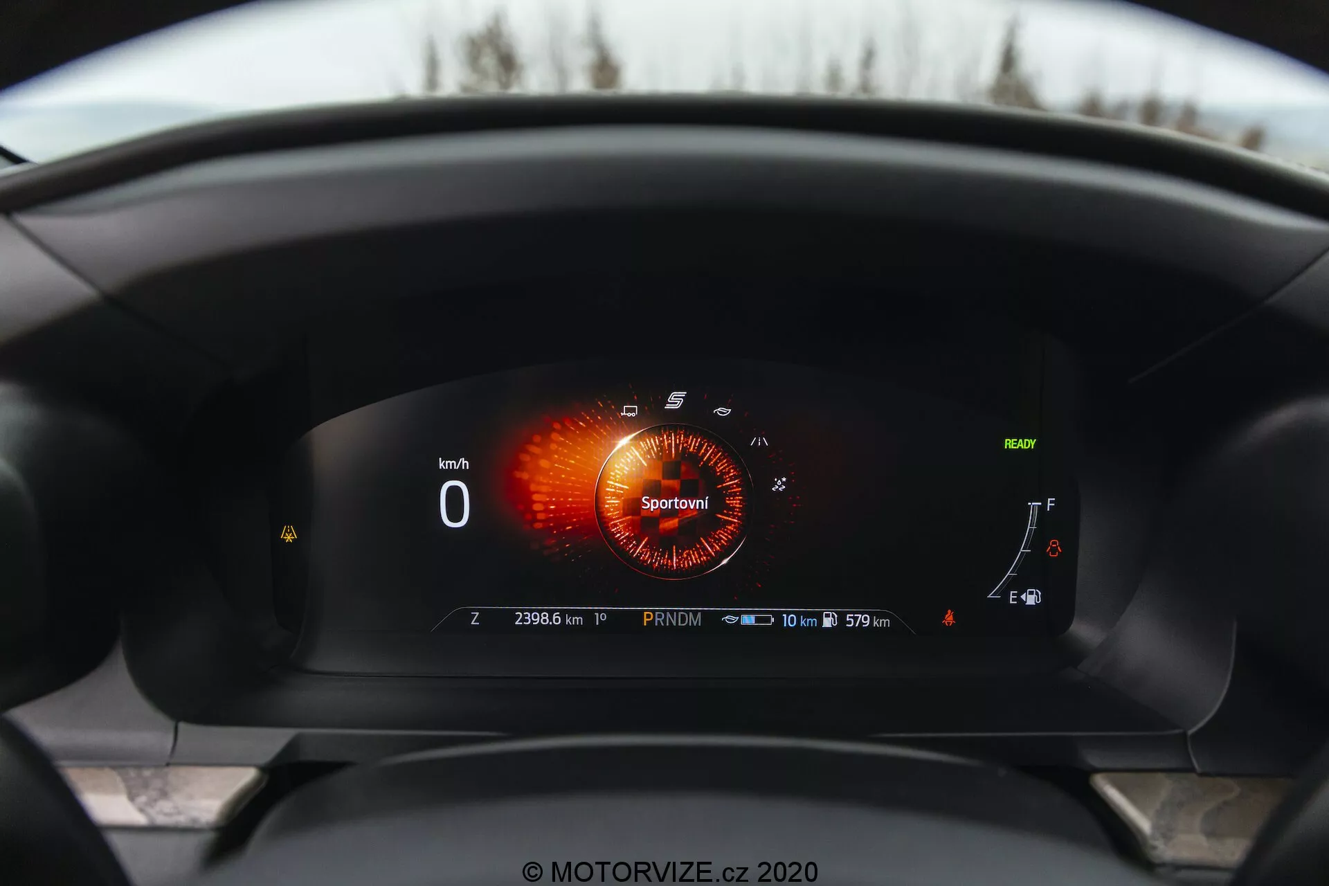 Interiör vy av en 2019 Ford Explorer från förarens perspektiv, med fokus på en helt digital instrumentpanel. Den digitala skärmen visar en varvräknare i 'Sport' läge med röd-orange grafik, en hastighetsmätare som visar '0 km/h,' en nästan full bränslenivåmätare, en kylvätsketemperaturmätare längst ner och olika indikatorer. Ett anmärkningsvärt inslag är en symbol för adaptiv farthållare, en servicemeddelande som läser '10 000 km eller 365 dagar,' och en vägmätare på '23063 km,' vilket indikerar att bilen är stillastående i 'Park' läge. En nästan full batteriikon antyder hybrid- eller elektriska möjligheter.