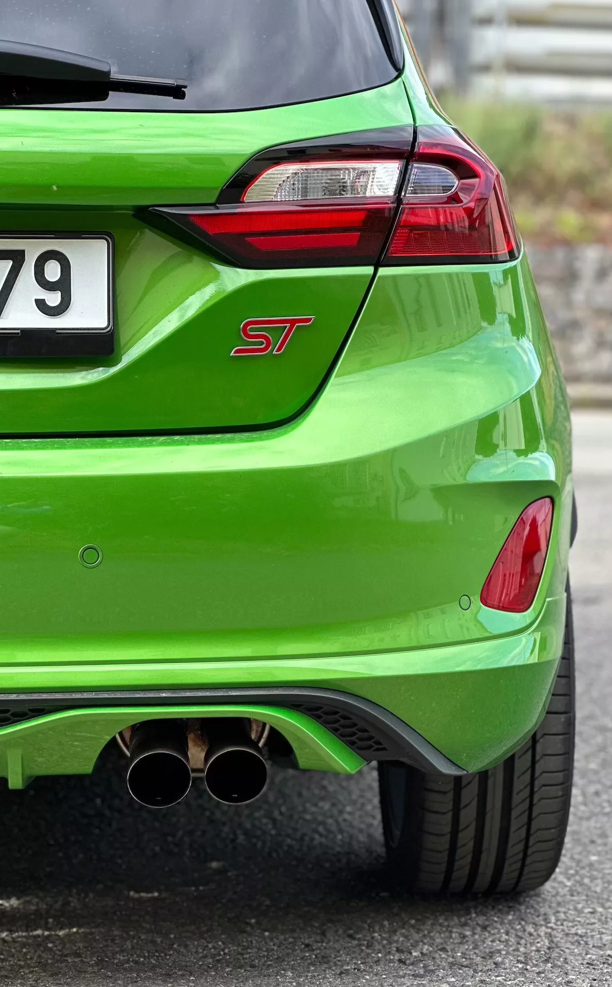 Närbild av baksidan på en 2022 Ford Fiesta ST i ljusgrön metallfinish, visar LED-bakljus, dubbla krom avgasrör och aerodynamisk bakre diffusor