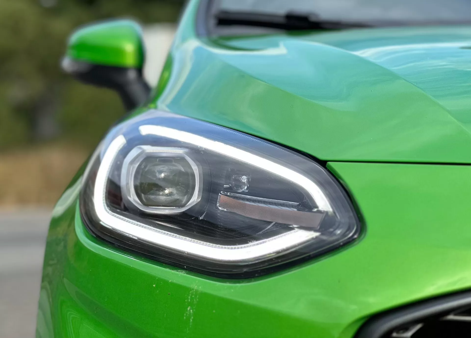 Närbild av vänster framsida på en Ford Fiesta 2022 i livlig grönt, som visar modern strålkastardesign, del av grillen och glansig finish med oskarp bakgrund som framhäver fordonets designdetaljer och avancerad belysningsteknik.