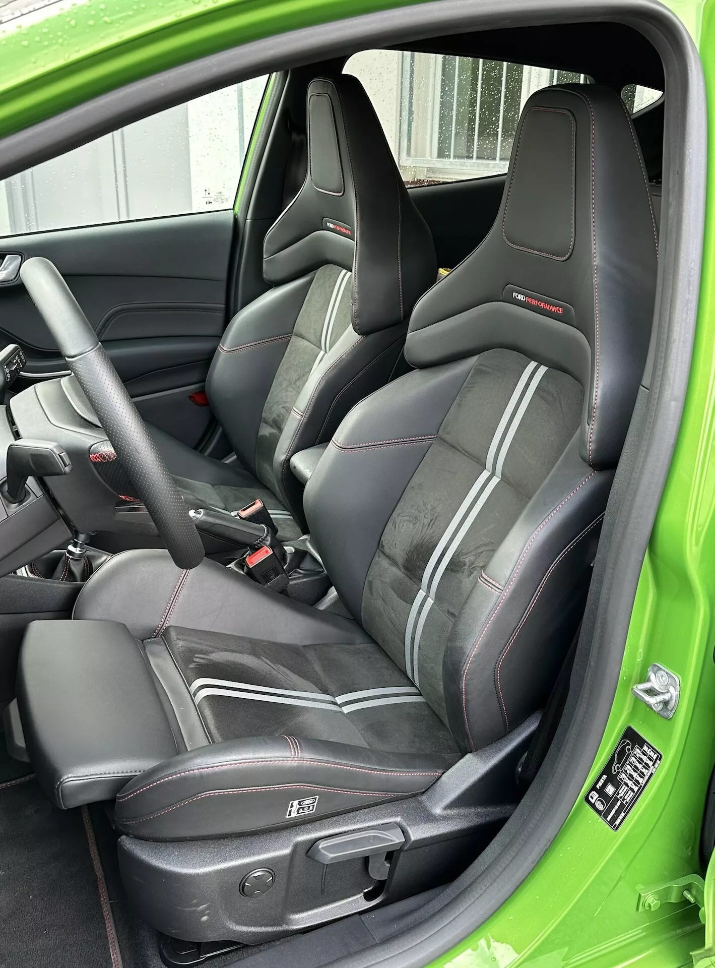Närbild på 2022 års Ford Fiesta sportiga förarsäte klätt i läder med röda detaljer, trepunkts säkerhetsbälte och elektrisk säteskontroll, accentuerad med en grön interiörinredning.