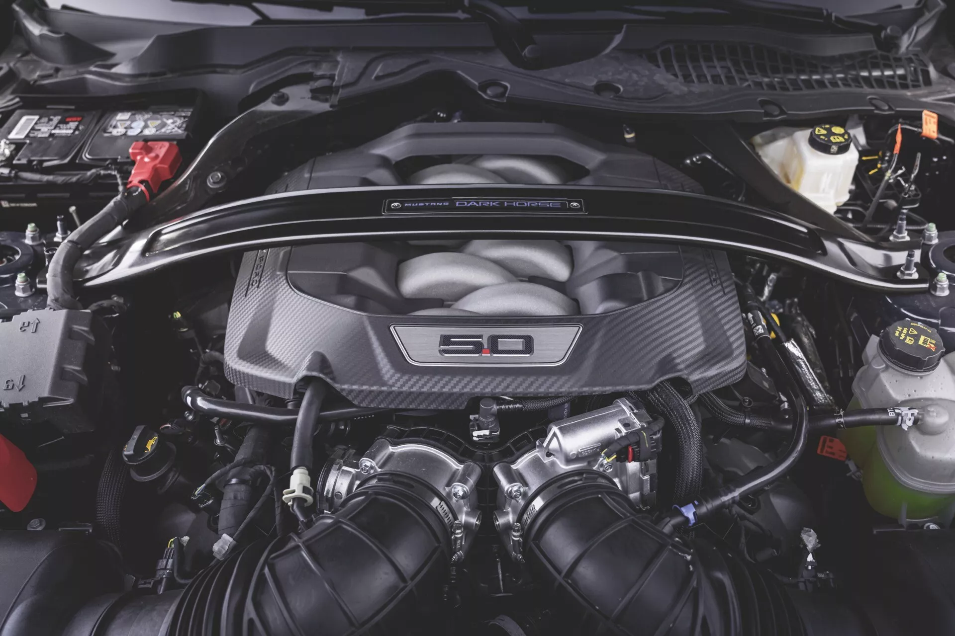 Närbild av motorutrymmet i en Ford Mustang 2:a generation 2024 med en 5,0 liters V8-motor, kolfiber motorlock, vätskereservoarer och elektrisk kabeldragning