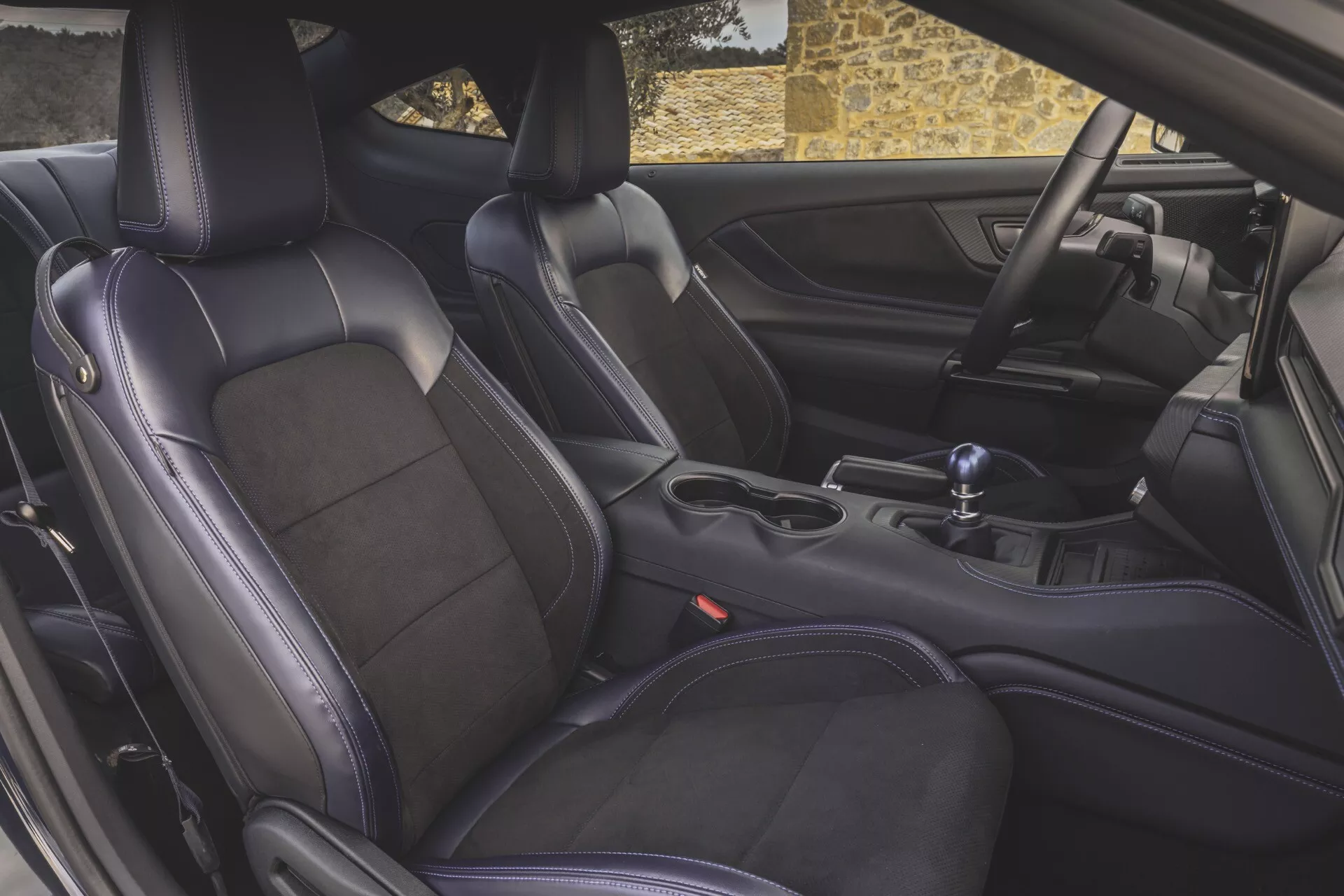 Detaljerad interiör vy av 2024 Ford Mustang som fokuserar på premium lädersportstolar, manuell växelspak och mittkonsol från förardörrens perspektiv