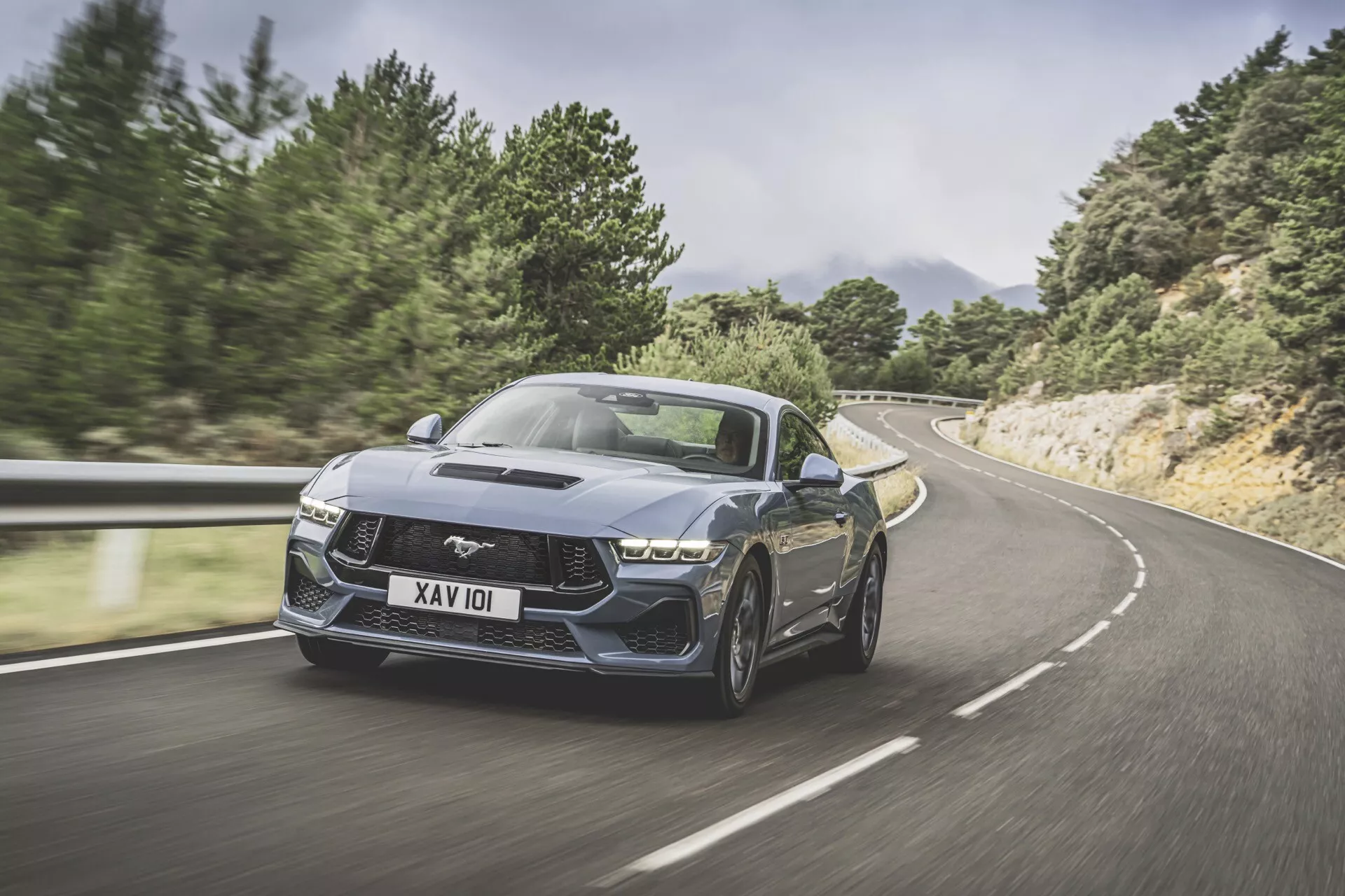 2024 Ford Mustang andra generationen i rörelse på slingrande väg, visar främre trekvarts vy, dynamisk hållning, aggressiv design och prestandaegenskaper