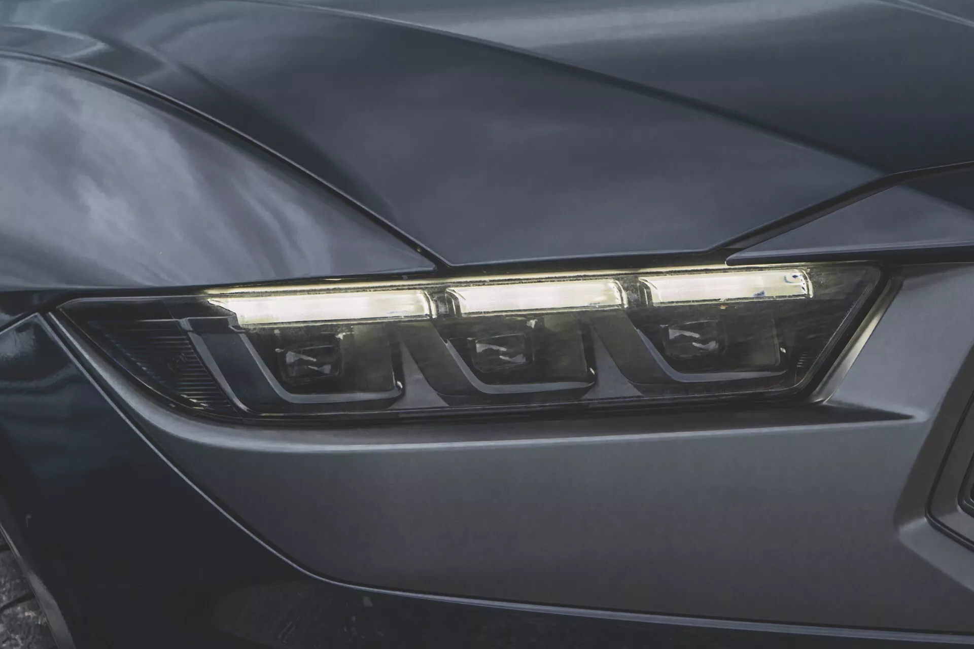 Närbild av förarsidans strålkastare på Ford Mustang 2024, som visar modern LED- eller HID-teknik och aerodynamisk design i en mörkfärgad finish.