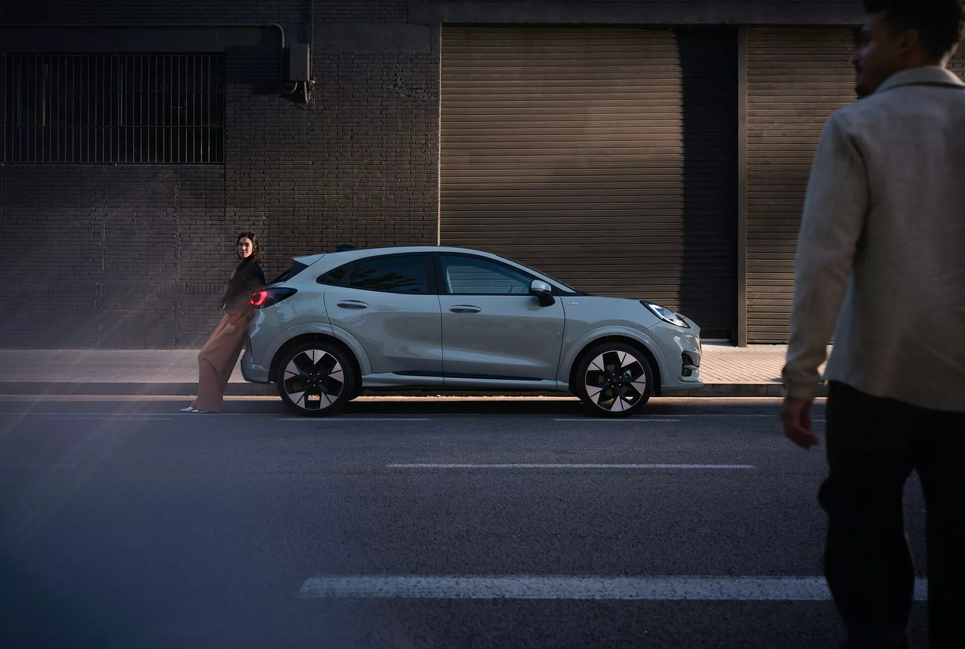 Ford Puma 2024 (II-facelift) halvkombi i metalliskt silver med en sportig design, fångad från en gatunivåperspektiv som visar dess slanka profil och moderna funktioner som svarta trimdetaljer och flerspåkiga hjul mot en urban bakgrund
