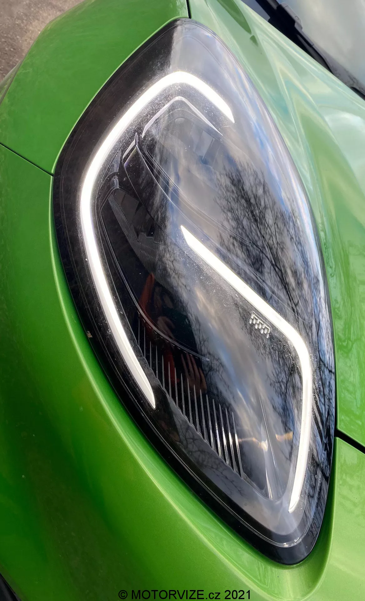 Närbild av vänstra strålkastarens montering på en livfullt grön Ford Puma ST 2020. Bilden visar strålkastarens eleganta och kantiga design ur en sned vinkel, och framhäver dess moderna LED-element och den glansiga, reflekterande lacken.