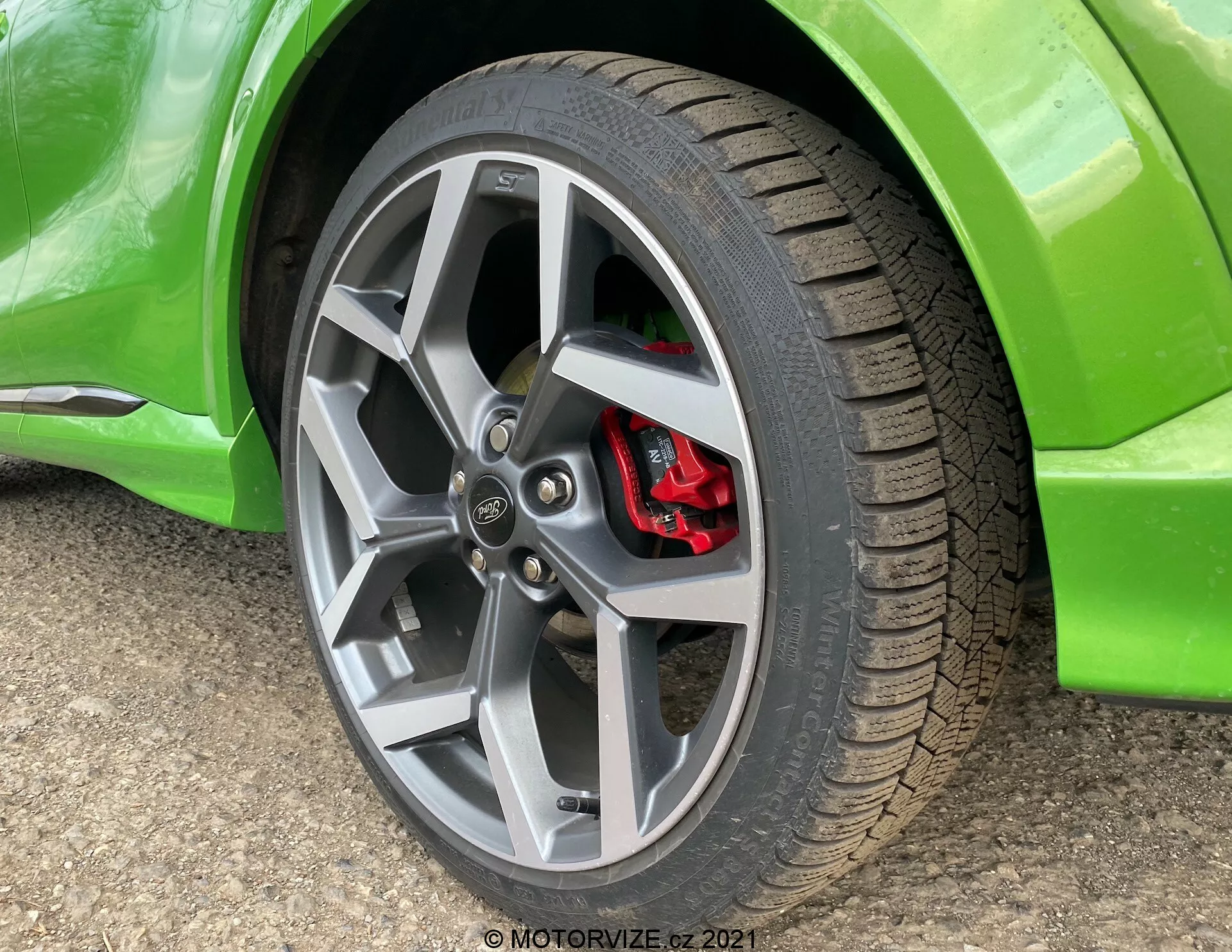 Detaljerad närbild av hjulet på Ford Puma 2020, med en flerspåkig fälg i legering med silverfinish, en vägavställd däckmönster och en rödpresterande bromsok delvis synlig bakom ekrarna. Fordonets klara gröna, glansiga kaross nära den böjda skärmen är också synligt.