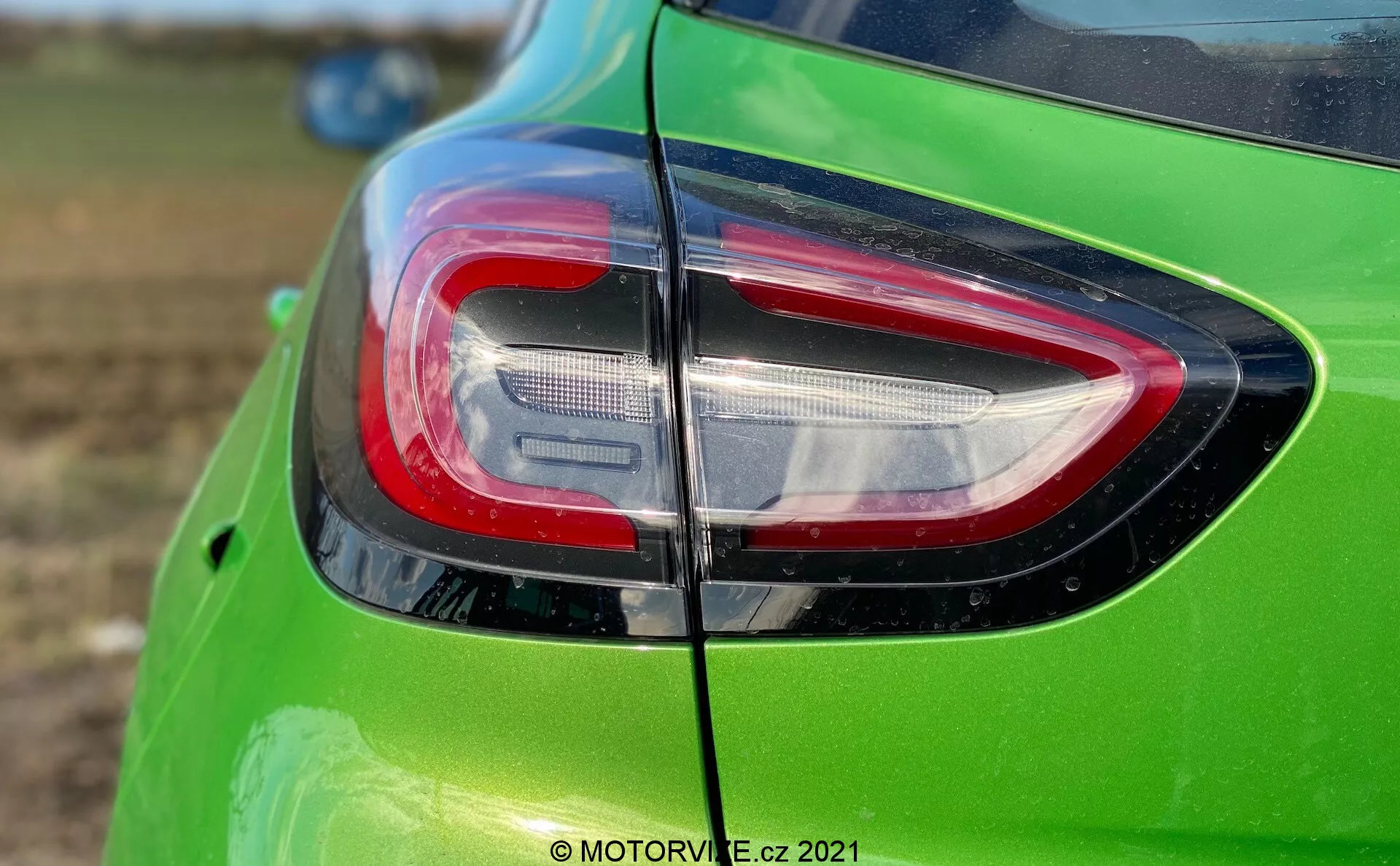 Närbild på den bakre delen av en ljusgrön Ford Puma 2020, med fokus på baklyktan på vänster sida. Den moderna designen har klara vita element för backljusen och röda element för bromsljusen, allt inneslutet i en boomerang-formad lins. Bilden, tagen från en något upphöjd vinkel, betonar skiljelinjen för bakluckan, vilket tyder på att det är en hatchback-modell. Baklyktan innehåller LED-element för förbättrad ljusstyrka och energieffektivitet, vilket betonar modern fordonsdesign.