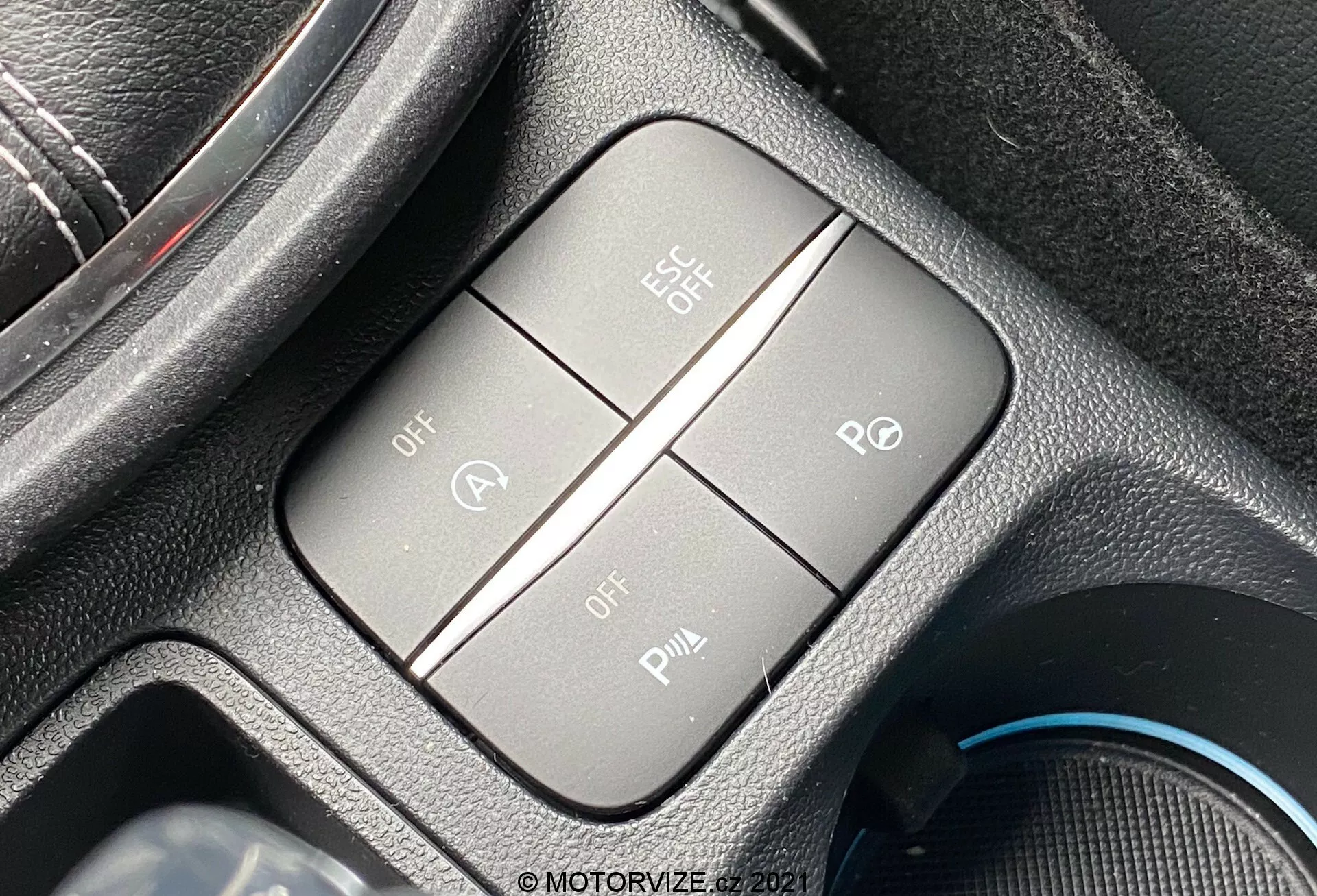 Närbild på 2020 års Ford Puma ST:s kontrollknappar fokuserade på körassistanssystem, fotograferade från en lätt lutad toppvinkel mot förarsätet. Kontrollpanelen inkluderar fyra taktila, eventuellt bakgrundsbelysta, knappar arrangerade i en kvadratisk formation inom en rektangulär ram. Den övre vänstra knappen, märkt 