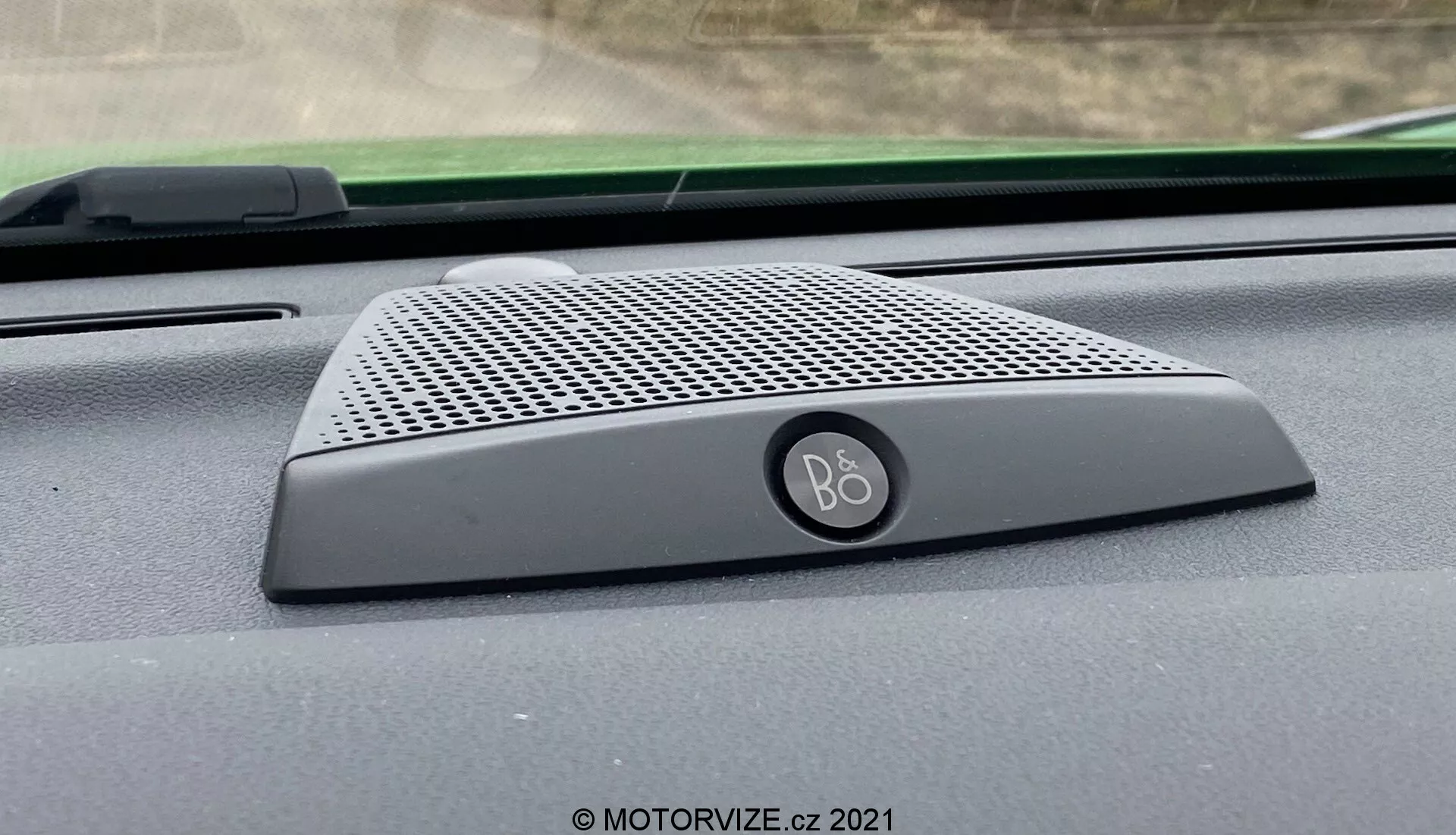 Närbild inifrån av 2020 Ford Puma ST:s instrumentbrädahögtalare med B&O (Bang & Olufsen)-logotyp, med en elegant design med fint perforerat galler och rundade kanter, placerad vid basen av vindrutan, vilket framhäver integrationen av premiumljudsystemet.