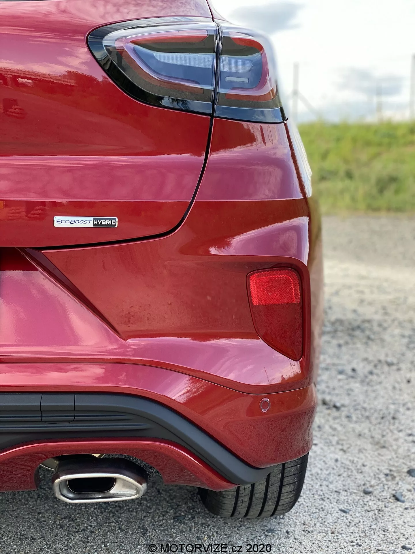 Bakre hörnvinkel av en röd Ford Puma 2020 tagen från nära håll, låg vinkel, med fokus på baksidans fenderkurvatur, bakljuselement, EcoBoost Hybrid-märke som indikerar hybridkraftdrivning och en enda kromavgaspipa. Framlyfter moderna designelement såsom skarpt vinklade bakljus och aerodynamisk bakre stötfångare med diffusorstyling.