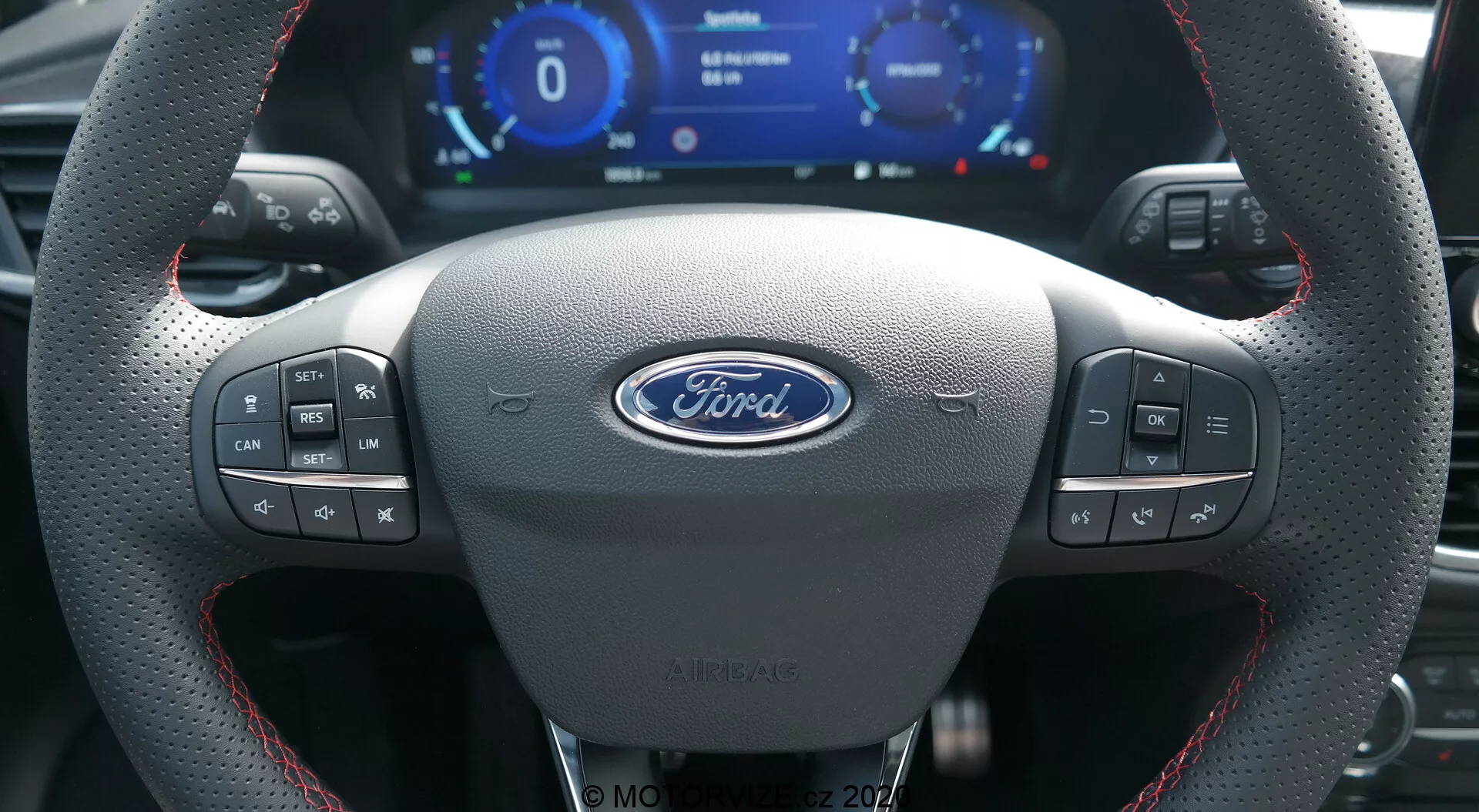 Interiören i en Ford Puma 2020 från förarens perspektiv som visar en sportig läderratt med röd söm, den centrala Ford-logotypen, flera kontrollknappar, en digital instrumentpanel med hastighetsmätare och varvräknare och metalliska växelspaddlar.