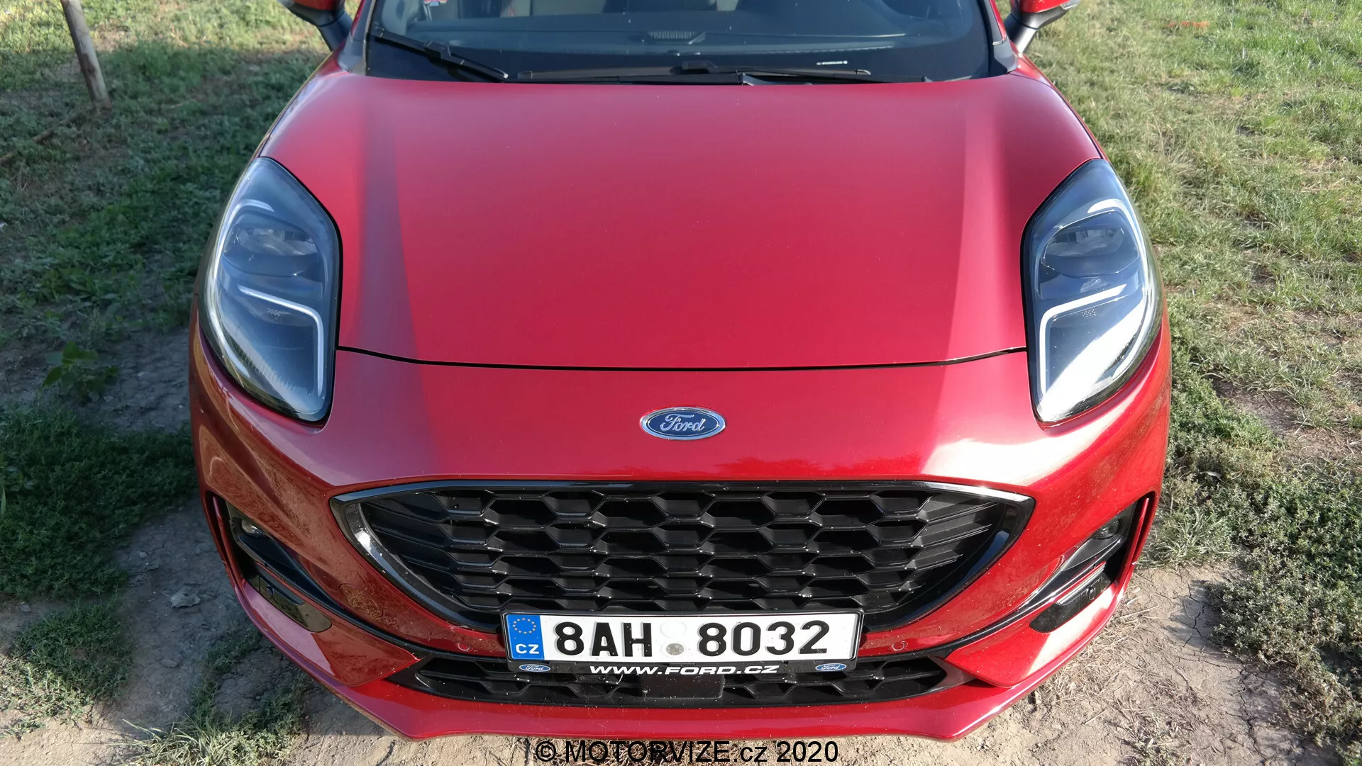 Frontal vy av en röd Ford Puma 2020 taget från en något upphöjd frontvy, med en kromkantad bikakgrill med Ford-logotyp, eleganta strålkastare med möjliga LED-element, slät konturerad motorhuv och en europeisk stil registreringsskylt som antyder att bilden togs i Tjeckien.