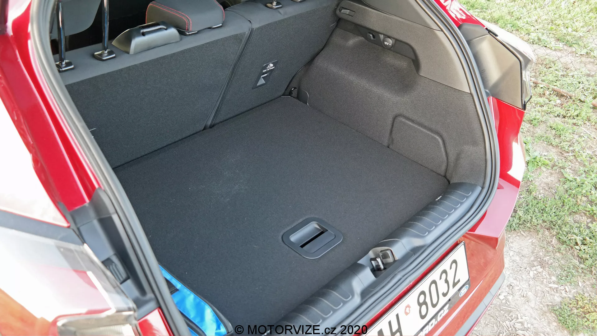 Bilden visar bakre utrymmet eller bagageutrymmet på en Ford Puma 2020. Fotot är taget från en vinkel något ovanifrån och från sidan, vilket ger en tydlig vy över bagageutrymmets rymliga inre och dess tröskel. Den mörka mattan antyder att den är utformad för att minimera synligheten av smuts. Inga lastföremål är synliga, vilket framhäver bagageutrymmets renlighet och rymlighet. Synliga egenskaper inkluderar sidofördjupningar eller fickor för förvaring av små föremål och en lastkrok eller fästpunkt för att säkra föremål. Bilens bakre ljusenhet är delvis synlig på bildens högra sida.