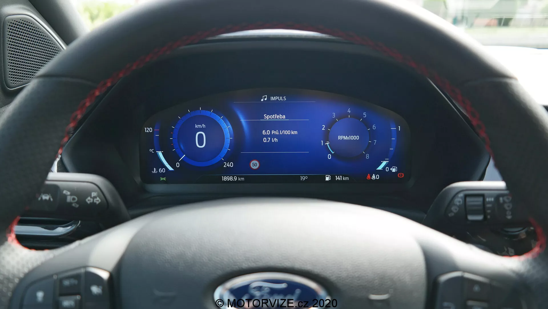 Interiörvy av 2020 Ford Puma från förarsätet, som visar en läderklädd ratt med multifunktionsknappar och en högupplöst digital instrumentpanel. Skärmen visar hastighet, navigation, fordonsdata, batterinivåindikator som antyder hybrid/elektriska möjligheter, och kontroller för media och farthållare.