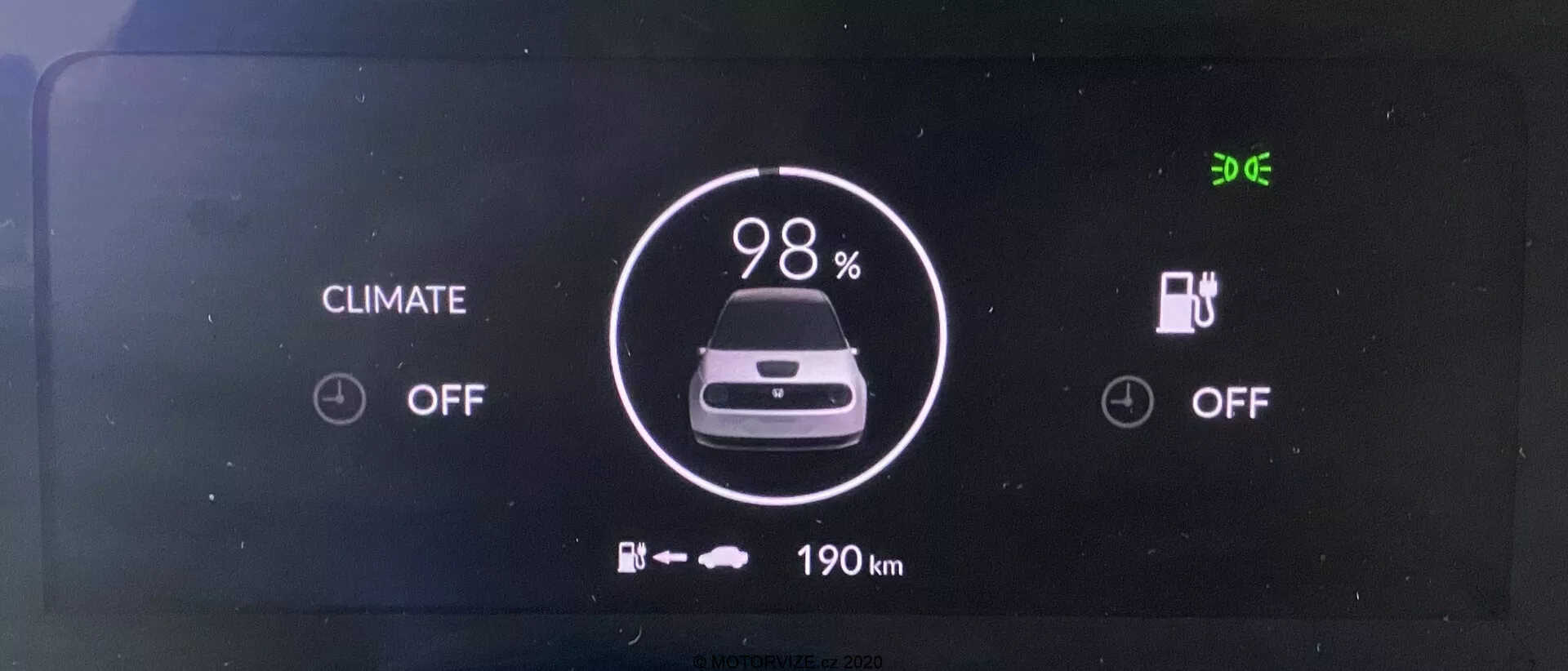 Digital instrumentpanel för 2020 års Honda e elbil. Skärmen, sedd rakt framifrån, visar tydligt en batteriindikator på 98% laddning, en bild av en bil och '190 km' återstående räckvidd under. Klimatkontroll- och laddningssystemen är båda 'OFF'. Tiden '9:06' visas i det övre vänstra hörnet.