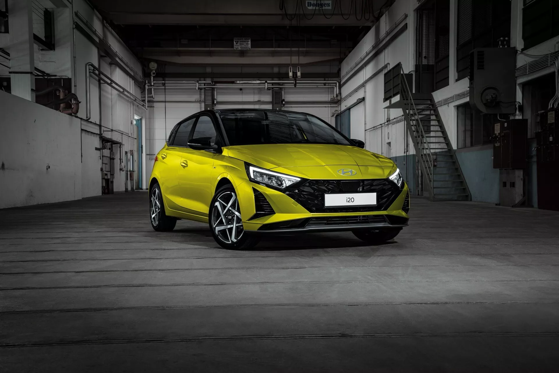 Hyundai i20 2023 (3:e generationens ansiktslyft) i en front tre kvartalsvy som visar dess moderna hatchback design, LED-strålkastare, sportig frontstötfångare och legeringshjul inne i ett industriellt lager med betonggolv och metall dörrar