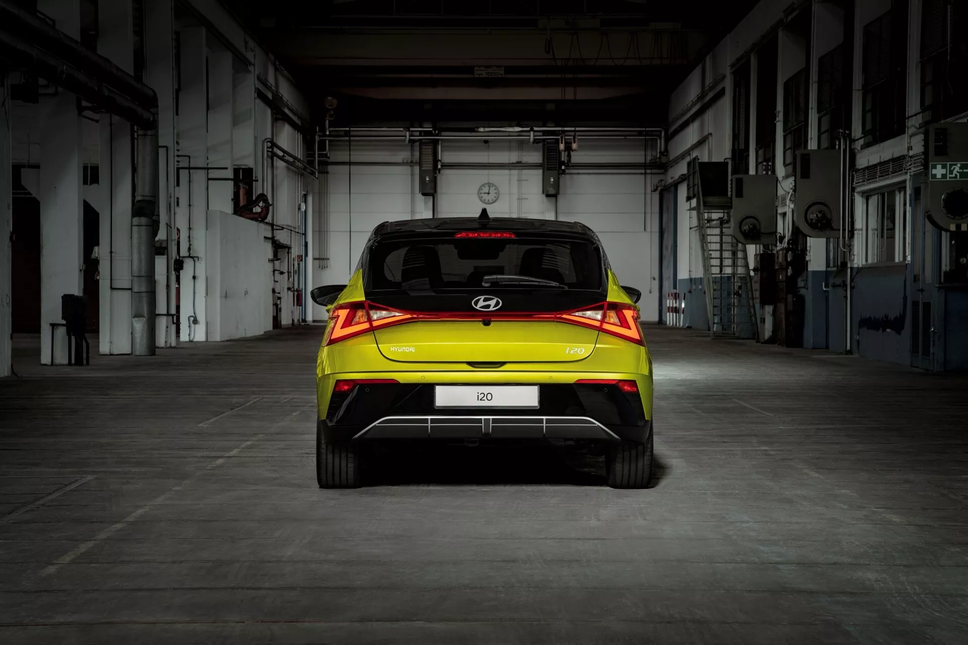 Bakvy av en Hyundai i20 2023 (3:e generationen-facelift) halvkombi med LED-bakljus och parkeringshjälp, framhävd i en industriell miljö