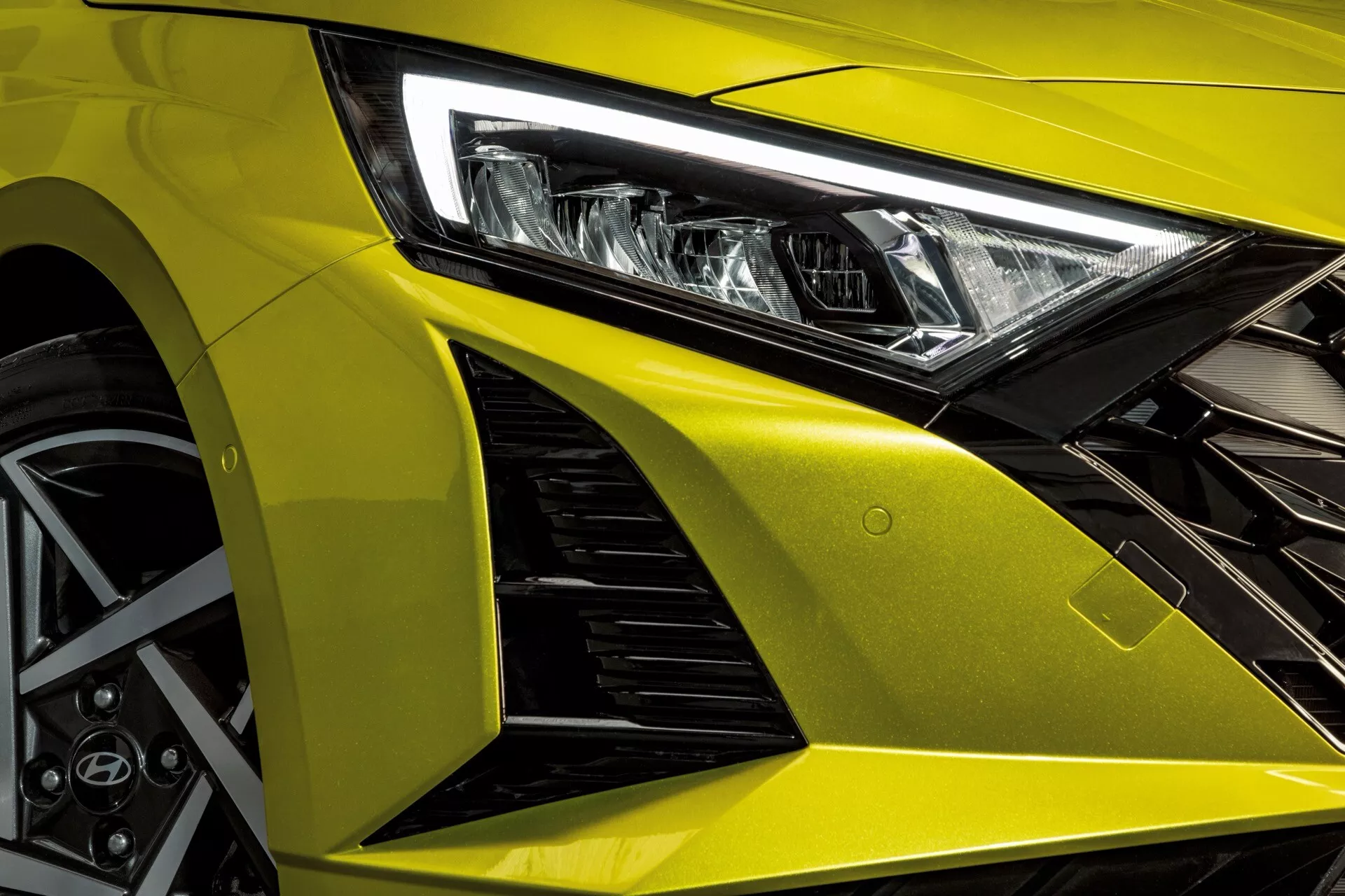 Framifrån vänster kvarts vy av Hyundai i20 2023, som framhäver dess aggressiva designlinjer, avancerade LED-strålkastare, metalliskt gul huva, aerodynamisk främre skärm med luftintag och sportig lättmetallhjul med prestandabromssystem