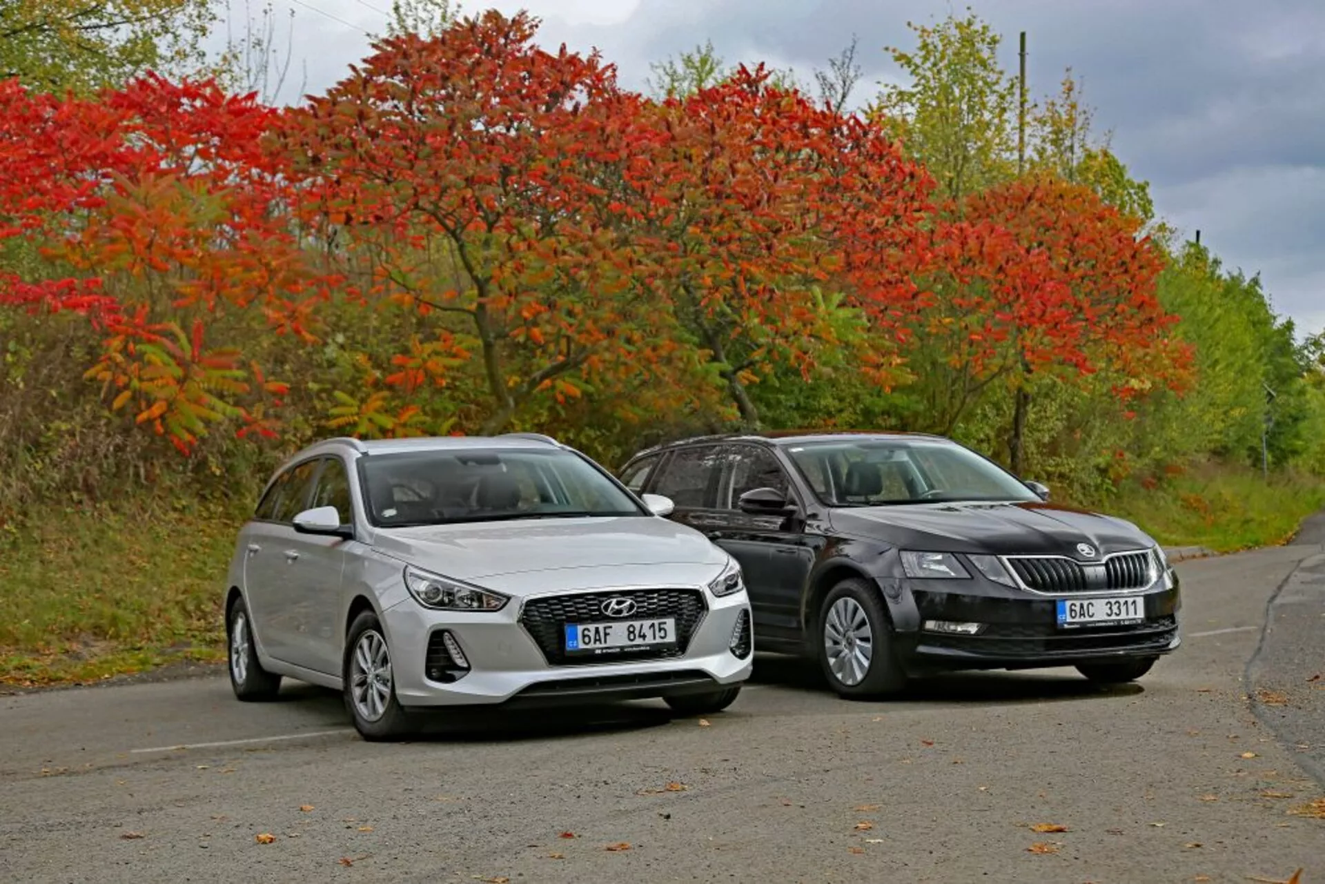 2017 års vit Hyundai i30 hatchback och mörkfärgad sedan sida vid sida på en lugn väg omgiven av höstvegetation, visar designlinjer och modern belysningsteknologi