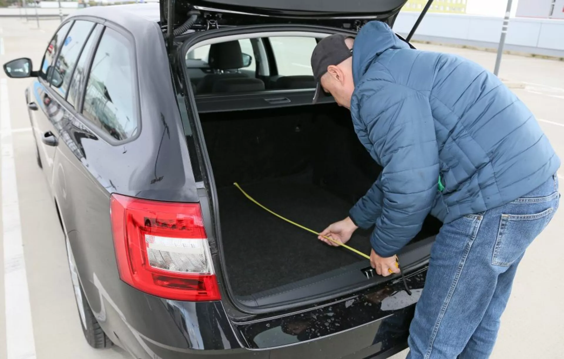 Hyundai i30 2017 (i30-N) som visar sitt rymliga bagageutrymme med invändig klädsel i tyg, har moderna LED-bakljus och en person som mäter bagageutrymmets storlek, fångad från en tredjedels vinkel i dagsljus utomhus