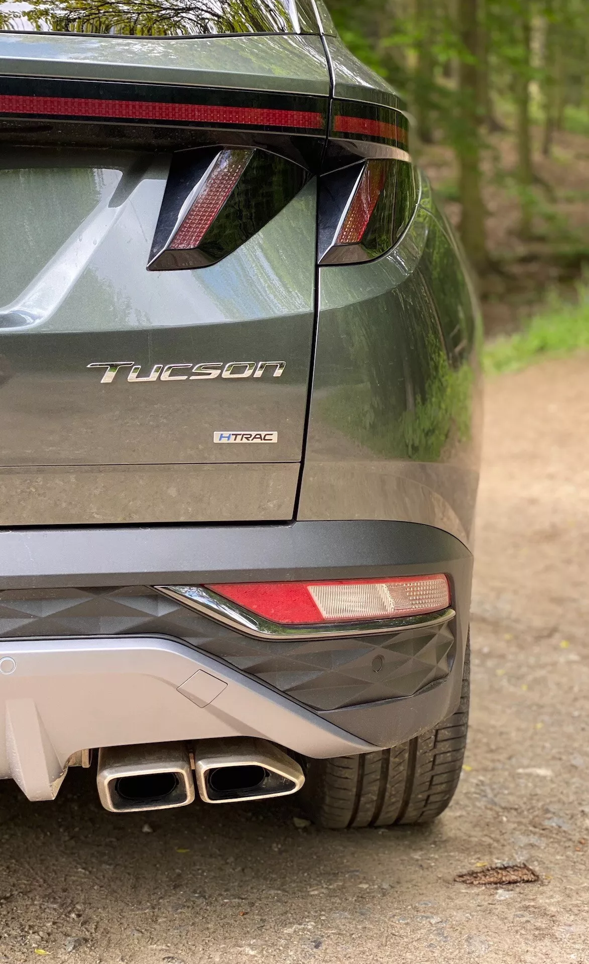 Delvis bakre vy av Hyundai Tucson 2020-modellen som indikerar att det är 1.6 T-GDi Pure-versionen, som visar högersidan av stötfångaren, del av bakljuset, bakspoilern med LED-bromsljus, dubbla avgasrör och modellmärkning med namnet 'Tucson' och motortekniken 'T-GDi'.