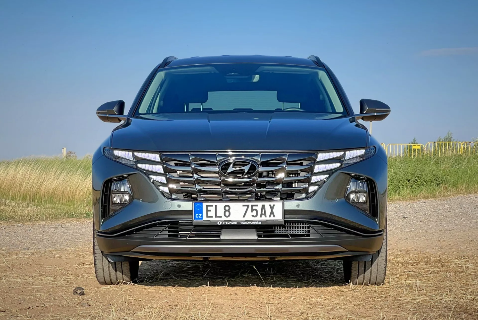 Frontvy av Hyundai Tucson 2020 som visar aerodynamisk huvtillverkning, kaskadgrill, skarpa LED-strålkastare och detaljerad stötfångare med möjliga teknikfunktioner, belägen på en naturbakgrund