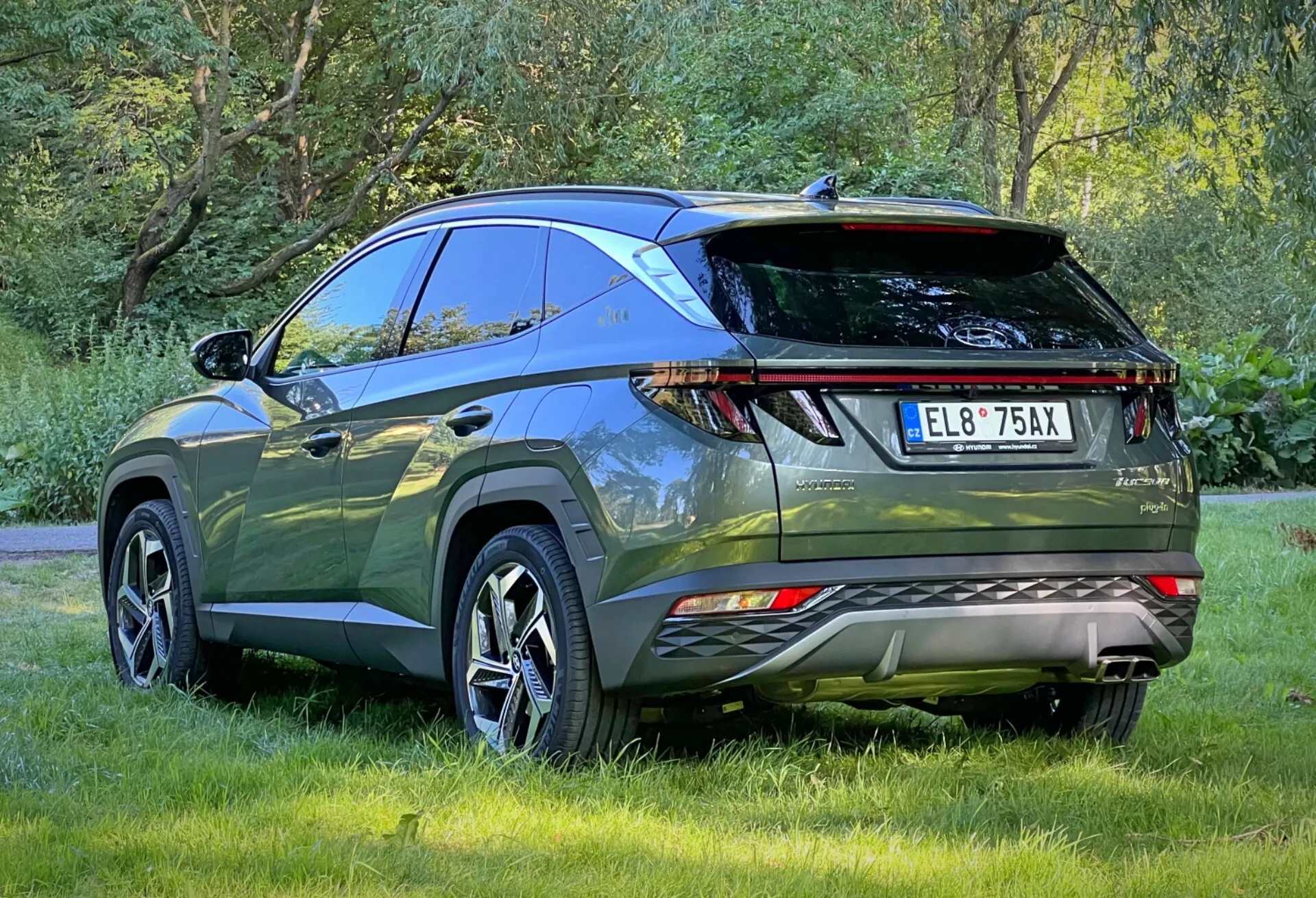 Bakre tre kvarts vy av Hyundai Tucson 2020 som framhäver LED-bakljus, parkeringssensorer, dubbla avgasrör, sportigt bakspoiler och takräcken, parkerad utomhus på gräs som visar en modern crossover SUV:s aerodynamiska design och avancerade funktioner för utomhusäventyr och praktisk användning.