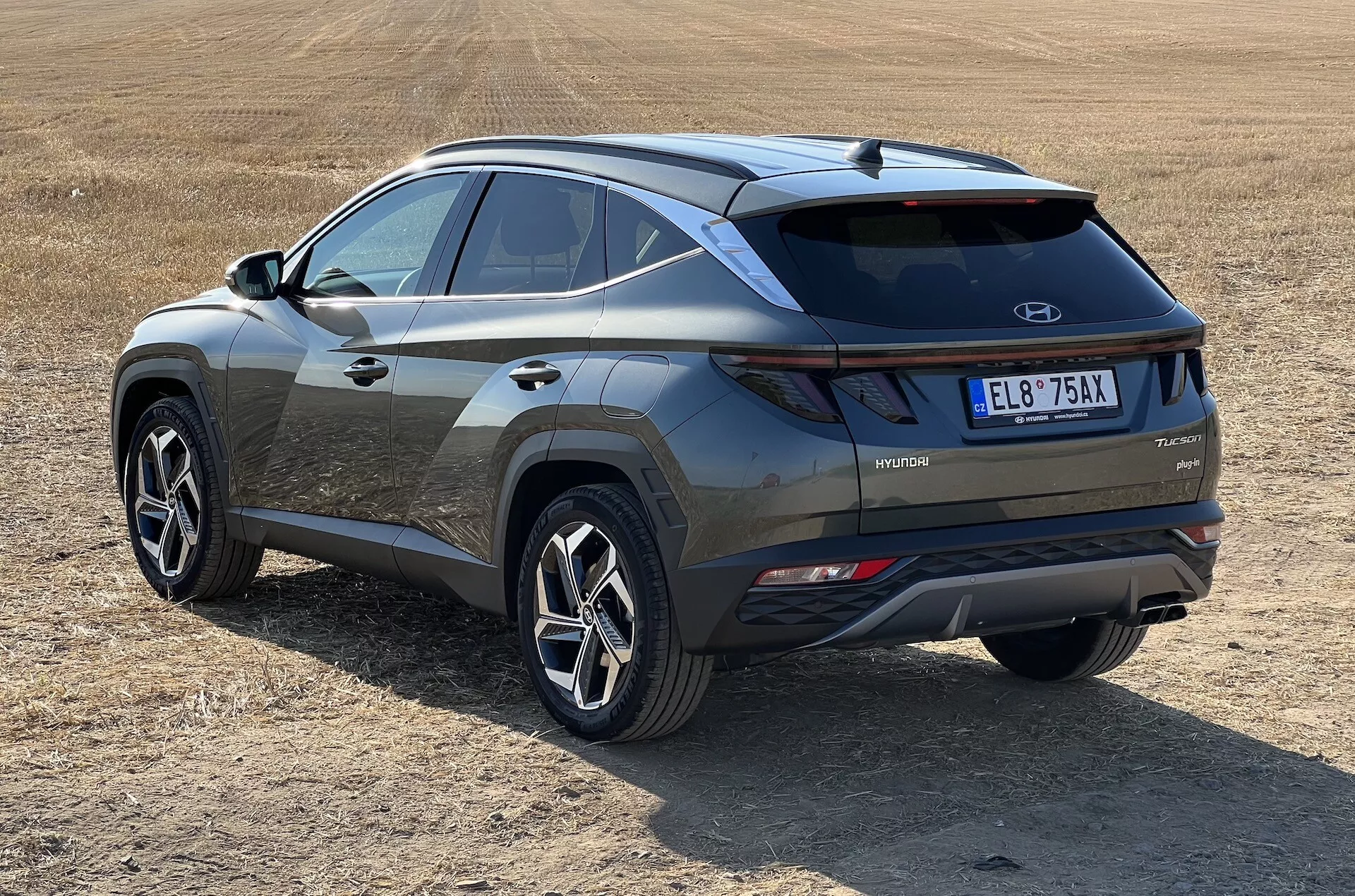 Moderna SUV Hyundai Tucson 2020 i snedvy showcasing bak- och sidoprofiler med hybridteknik märke på torrt gräsigt fält, belyser LED-bakljus, kontrasterande stötfångarinsats och sportiga flerspoke hjul