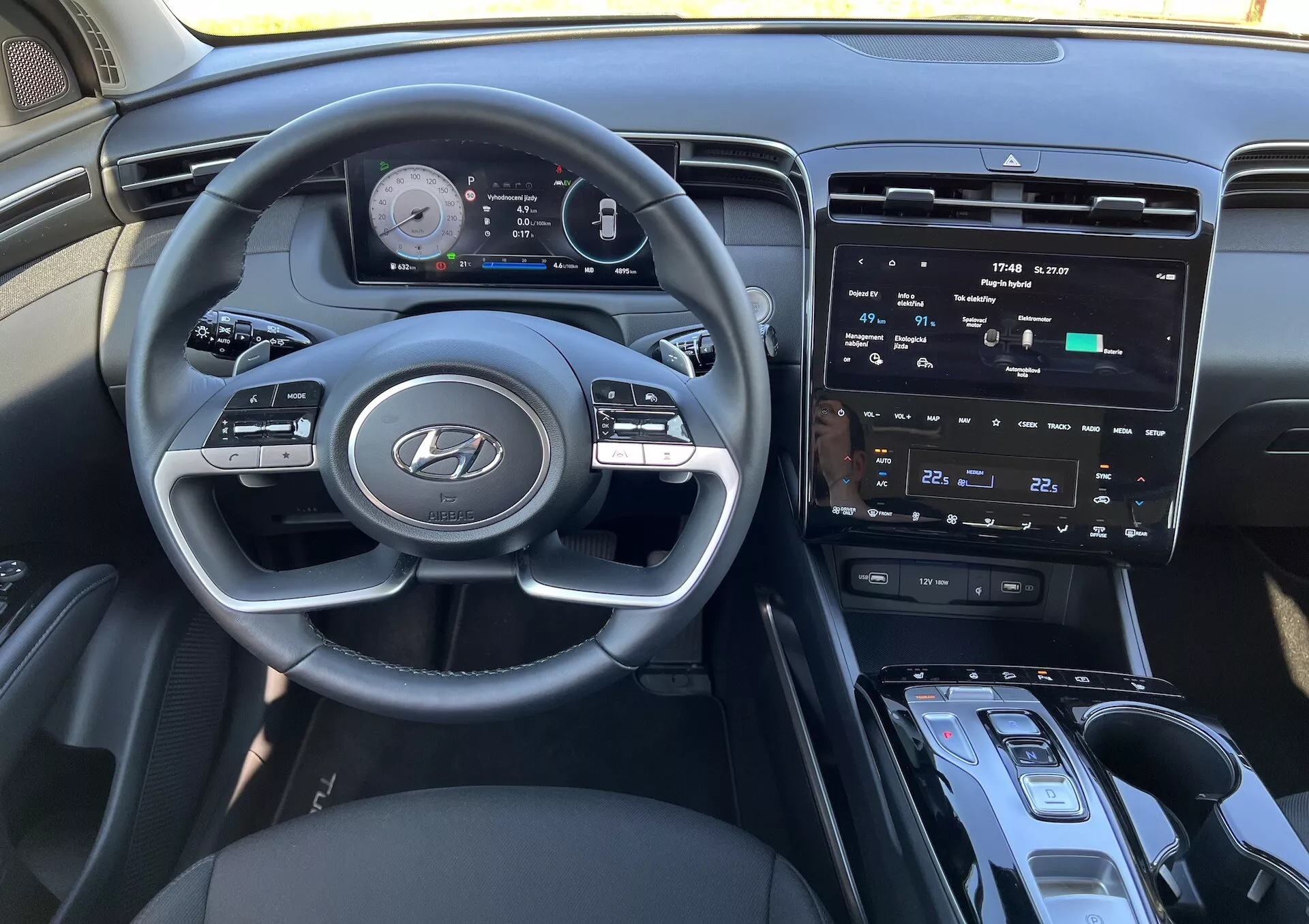 Interiör i Hyundai Tucson 2020 som visar ratten med Hyundai-logotypen, avancerad digital instrumentbräda, central pekskärm för infotainment, klimatkontroller, start/stopp-ignitionknapp, växelspak och möjligt trådlöst laddningsområde ur förarens perspektiv