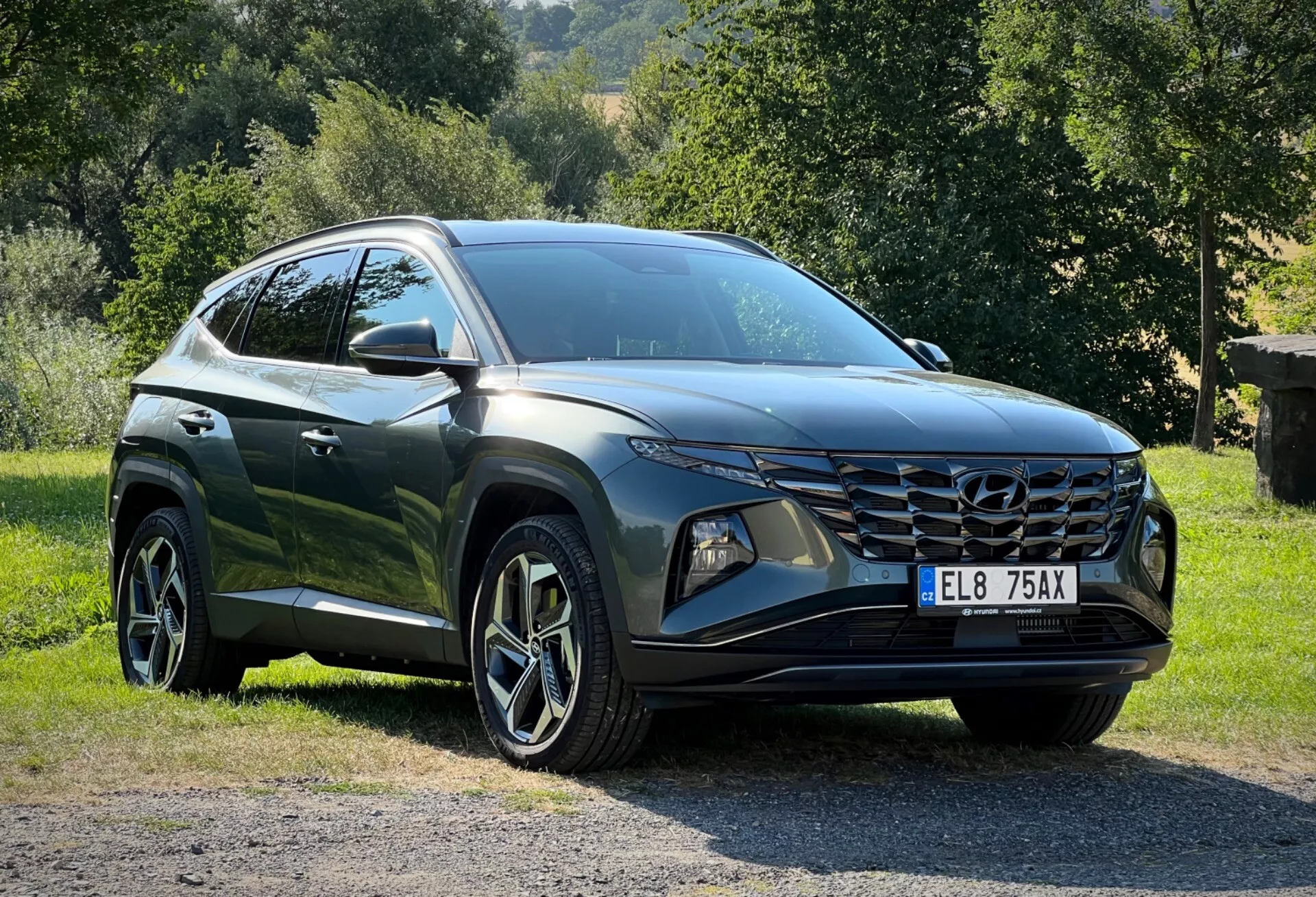 Hyundai Tucson 2020 parkerad på gräs med landsbygdsbakgrund, visar tre fjärdedels frontperspektiv för en detaljerad vy av dess eleganta LED-strålkastare, vinklad frontgrill och glansig mörkfärgad yta