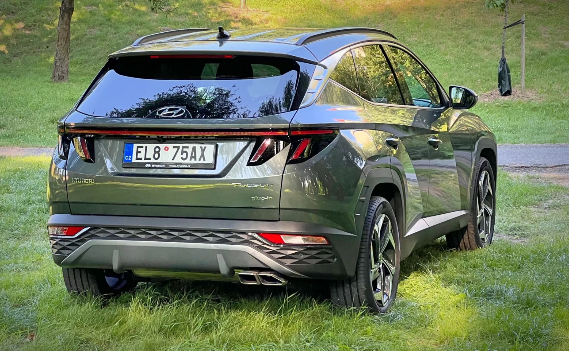 Trebjärtad bakvy av en Hyundai Tucson 2020, som visar dess LED-bakljus, aerodynamisk design med takspoiler och hajfenantenn, premium mörkgrön metallisk finish, och utrustad med stora legeringshjul och parkeringssensorer, i en crossover urban livsstil miljö