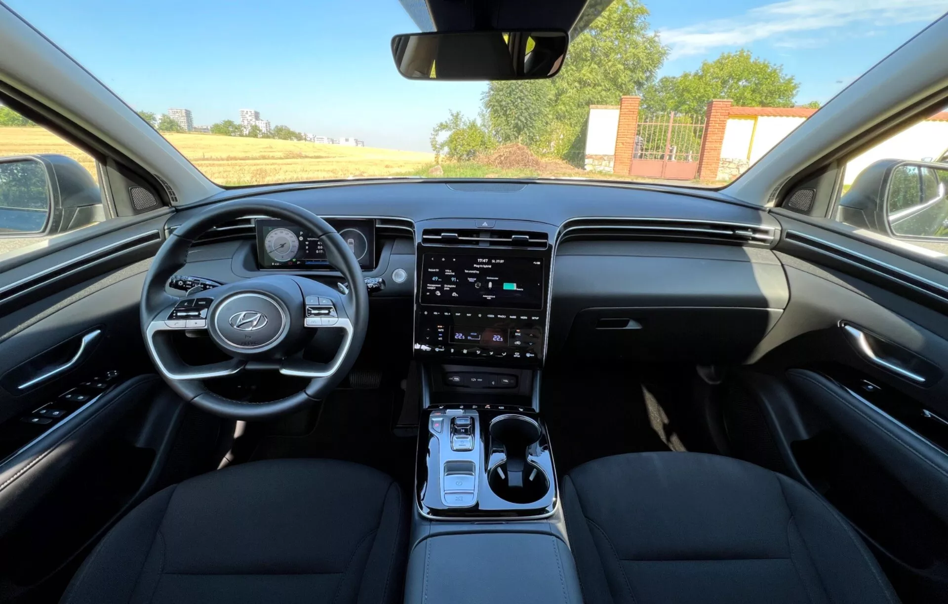 Interiör av Hyundai Tucson 2020 som visar framsäten, ratt med tillverkarens logotyp och kontrollknappar, digital instrumentkluster, vertikal pekskärmsinfotainmentsystem på mittkonsolen, automatisk växelspak, och tvåtonig instrumentbrädans design från en synvinkel som liknar förarens eller framsätespassagerarens perspektiv