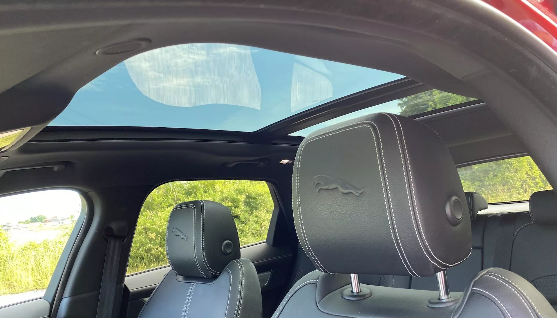 Interiör i Jaguar F-Pace 2021, sett från baksätet, med mörka lädersäten med vita sömmar, markerade nackstöd och ett panoramatak som släpper in naturligt ljus.