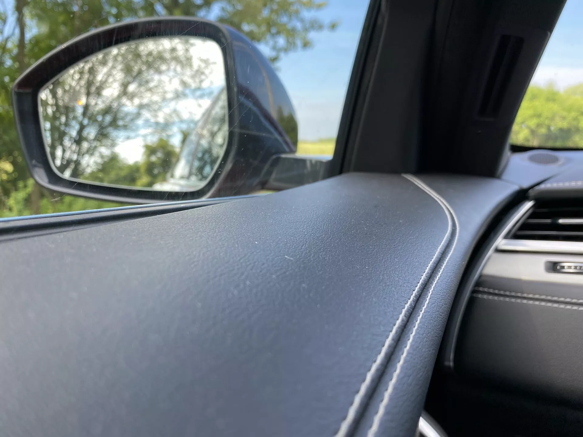 Interiörvy av 2021 Jaguar F-Pace fokuserad på förarsidan från låg vinkel, med betoning på instrumentbrädans struktur, dörrpanel och sidospegel