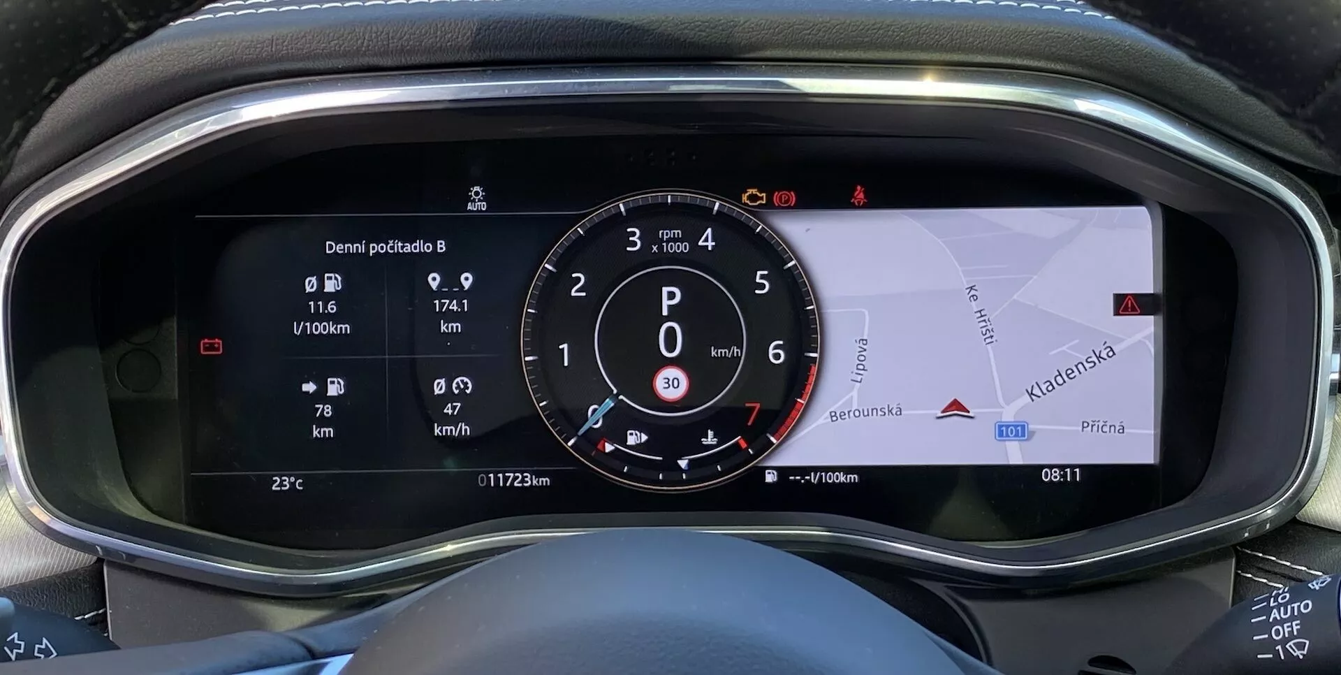 Närbild av den digitala instrumentpanelen i en Jaguar F-Pace 2021 med en stillastående hastighetsmätare som visar 0 km/h, bränsleeffektivitet på 9.7 L/100km, total körsträcka på 117420 km, trippmätare på 74.1 km, utomhustemperatur på 23°C, växel i läge Park 'P', aktiv Auto Start-Stop-system, varningsikon för öppen dörr och integrerad GPS-navigeringskarta.