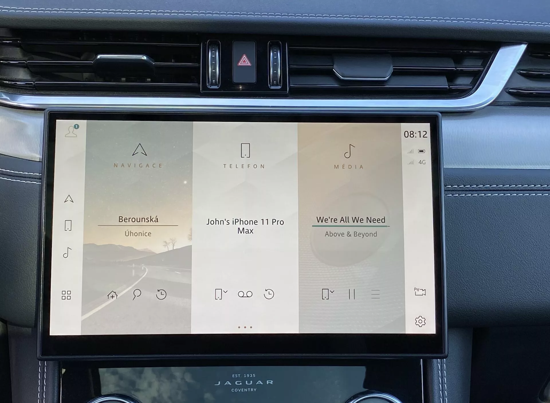 Närbild av infotainmentsystemets skärm inuti en Jaguar F-Pace 2021, som visar en snygg, modern display med tre huvudmenyalternativ: 'Navigate', 'Telephone' och 'Media'. Skärmen har ytterligare kontroller för mediefunktioner och visar tiden som 08:12 samt en utomhustemperatur på 4 grader Celsius. Gränssnittet är användarvänligt med tydlig text och stora tryckmål, placerat i en stilfull instrumentpanel med en borstad metalldekor.