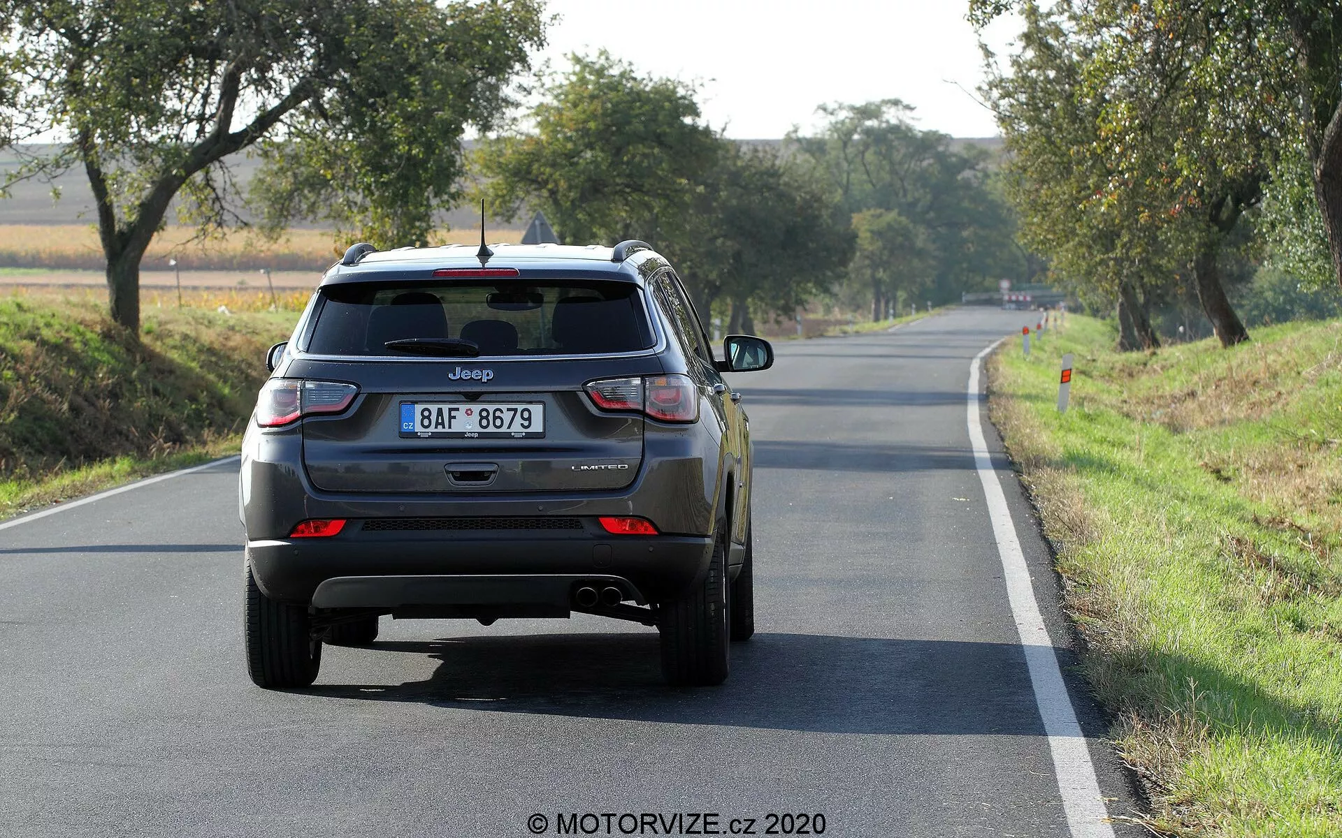 Bakifrån vy av en Jeep Compass SUV 2017 på en tvåfältsväg i dagsljus, synligt varumärke, modellnamn, europeisk stil registreringsskylt, LED-bakljus, stängd baklucka med bakrute torkarblad, tredje bromsljus på bakspoiler, bakre stötdämpare med reflexer, dubbla avgasrör på vänster sida, bakre aluminiumhjul, ytterligare märken som möjligen indikerar utrustningsnivå eller drivlina.